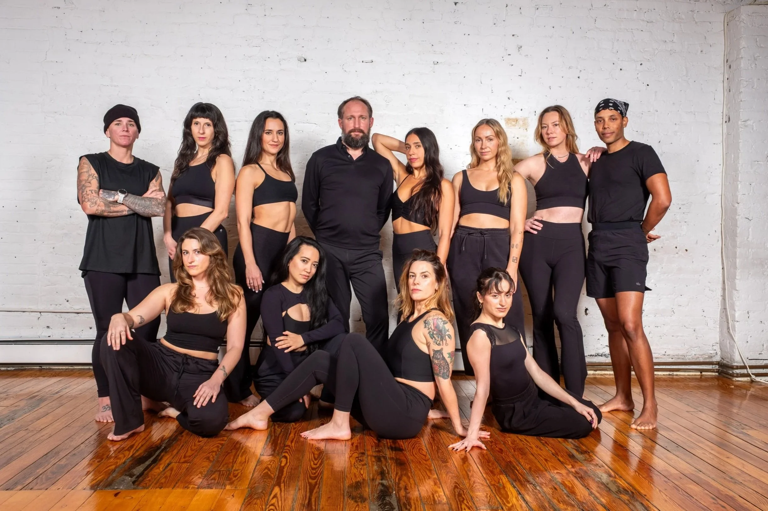 Full New Love City instructor team formal group portrait against a white brick studio wall