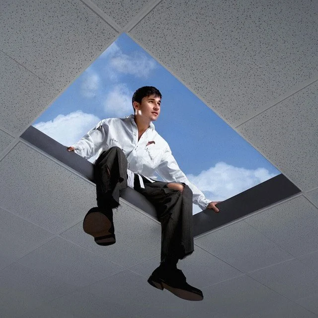 Instagram post: man in a white shirt sitting in a square ceiling skylight against blue sky