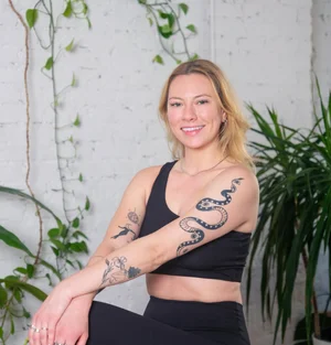 Instagram post: blonde instructor with a snake arm tattoo smiling against white brick with vines