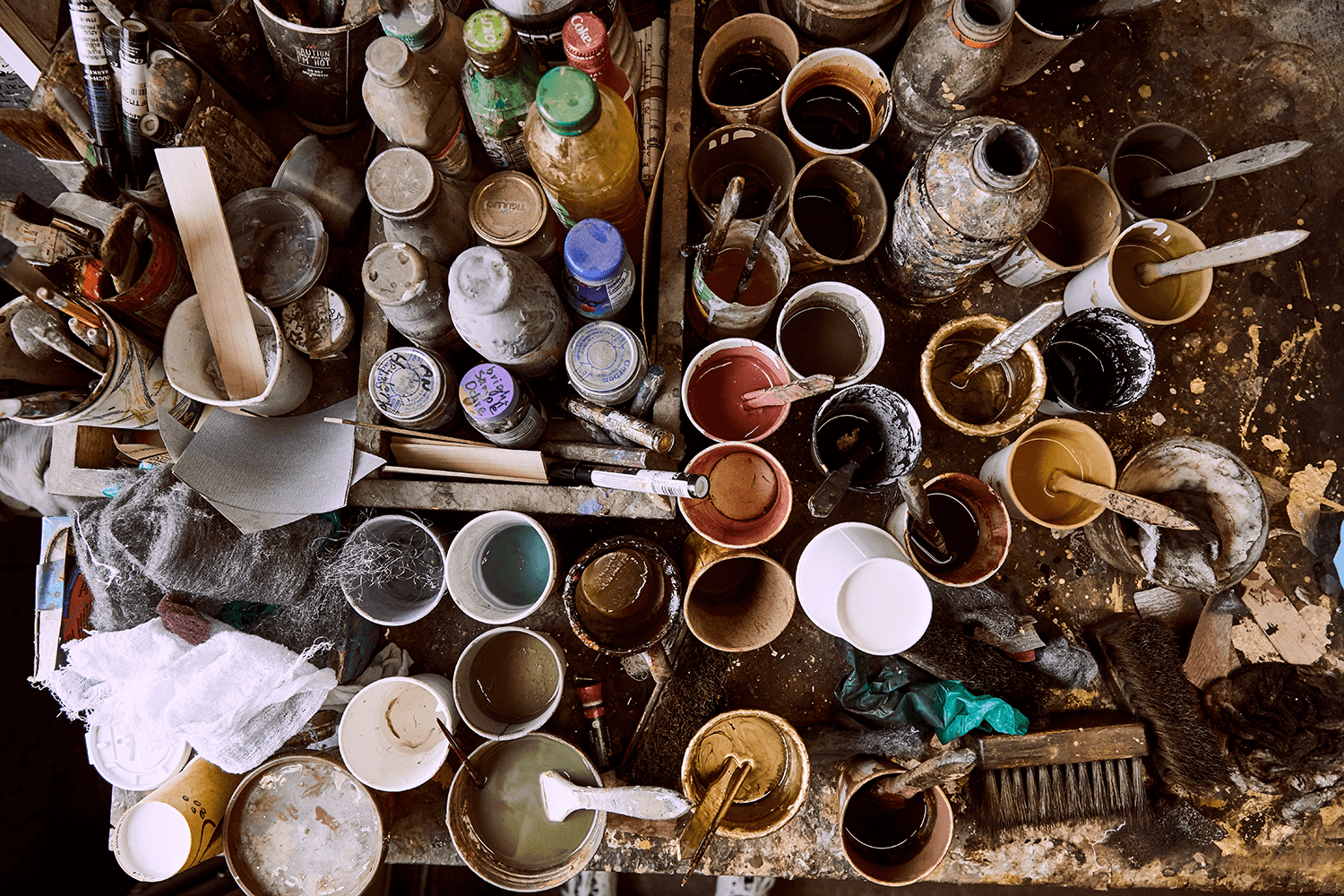 Overhead view of an artist's workbench covered in paint cans, bottles and brushes