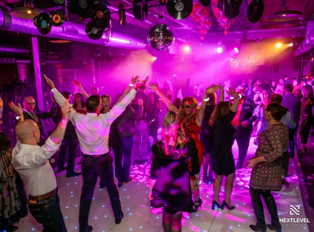 Corporate dance floor with guests dancing under pink and purple disco lighting and a mirror ball
