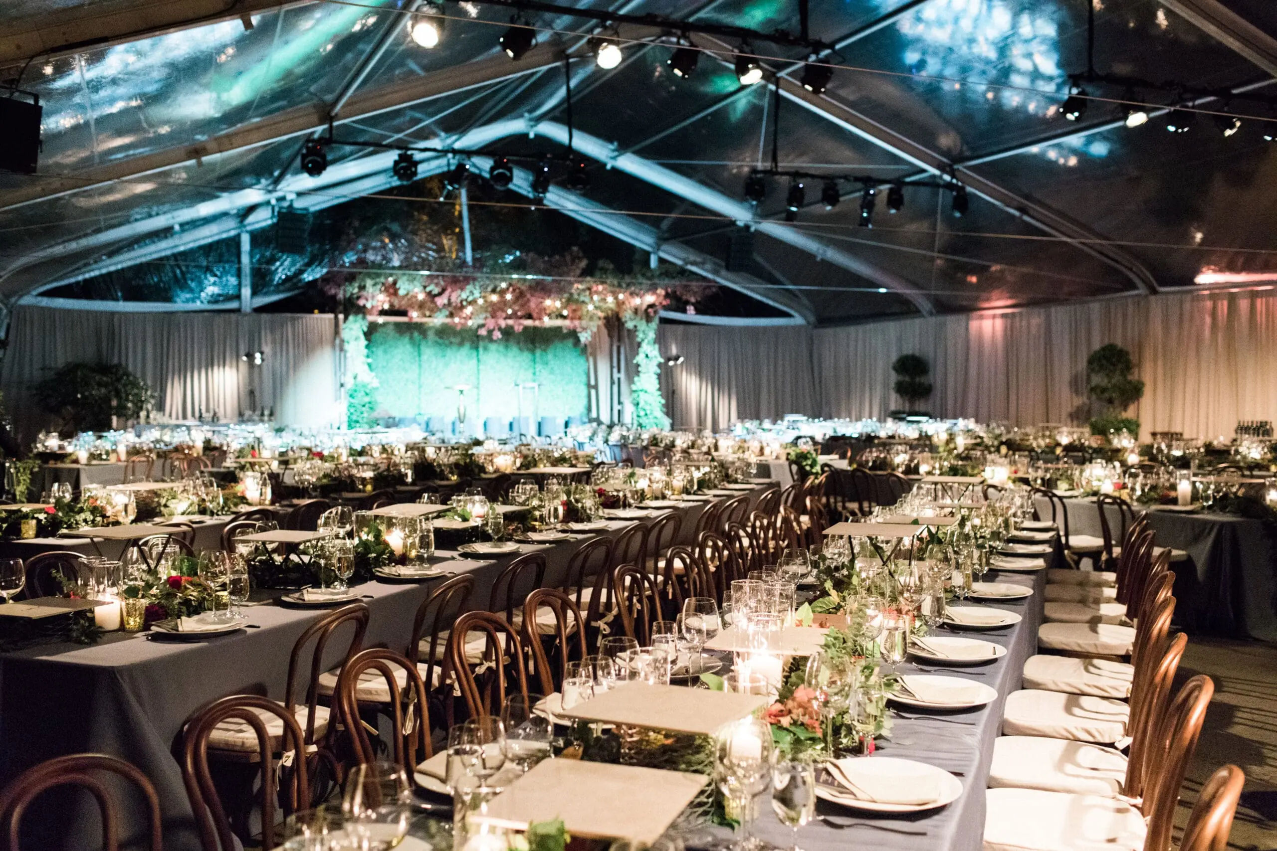 Elegant tented gala dinner with long tables of greenery, candles and glassware under a clear roof