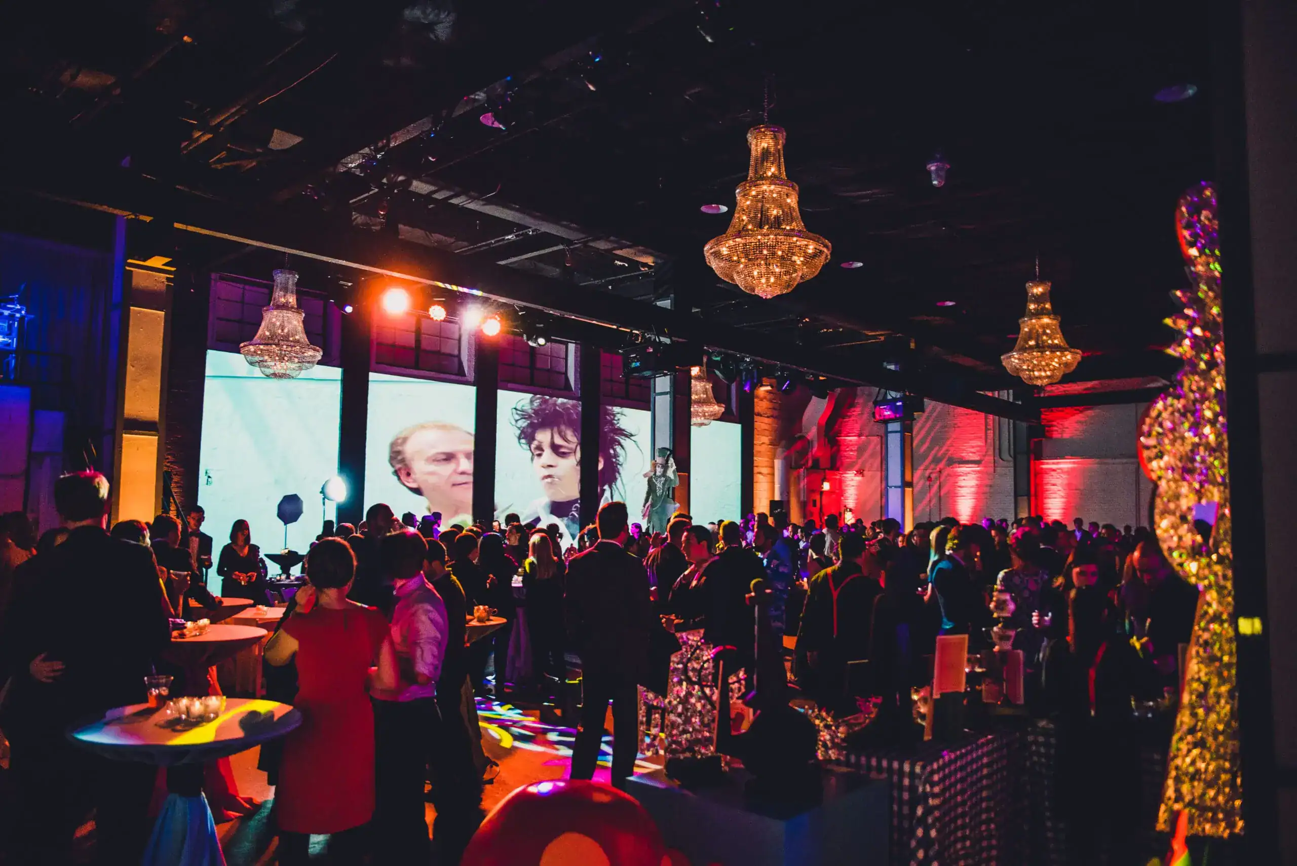 Large indoor experiential event with chandeliers, LED walls showing film imagery and a crowd of attendees