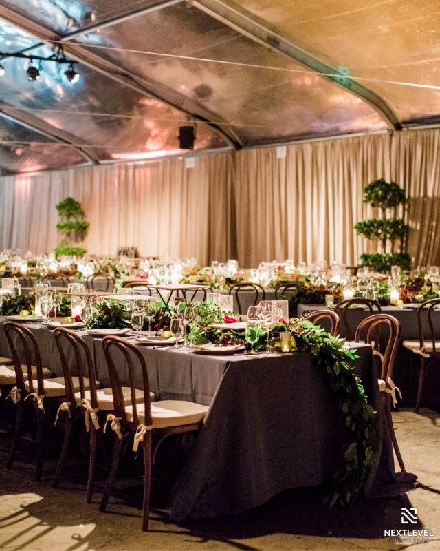 Tented gala dinner with long tables set with greenery runners and candles