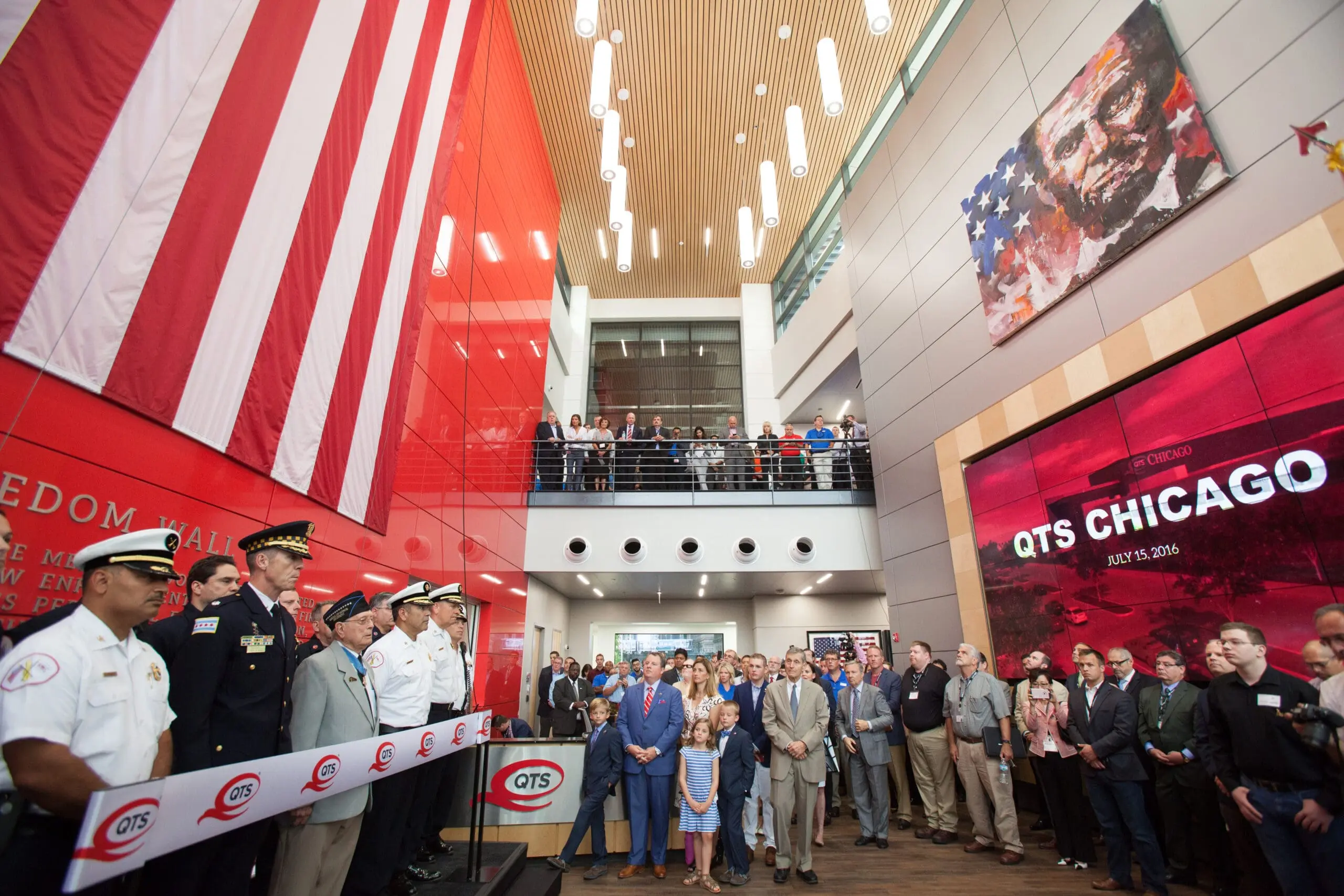 QTS Chicago building opening ceremony with officials, first responders and a large crowd in a modern atrium with a US flag
