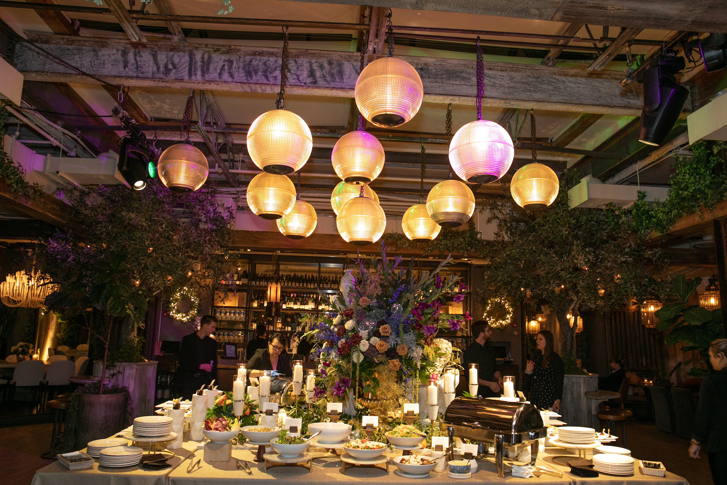 Indoor corporate dinner with globe pendant lights, a large floral centerpiece and a buffet spread