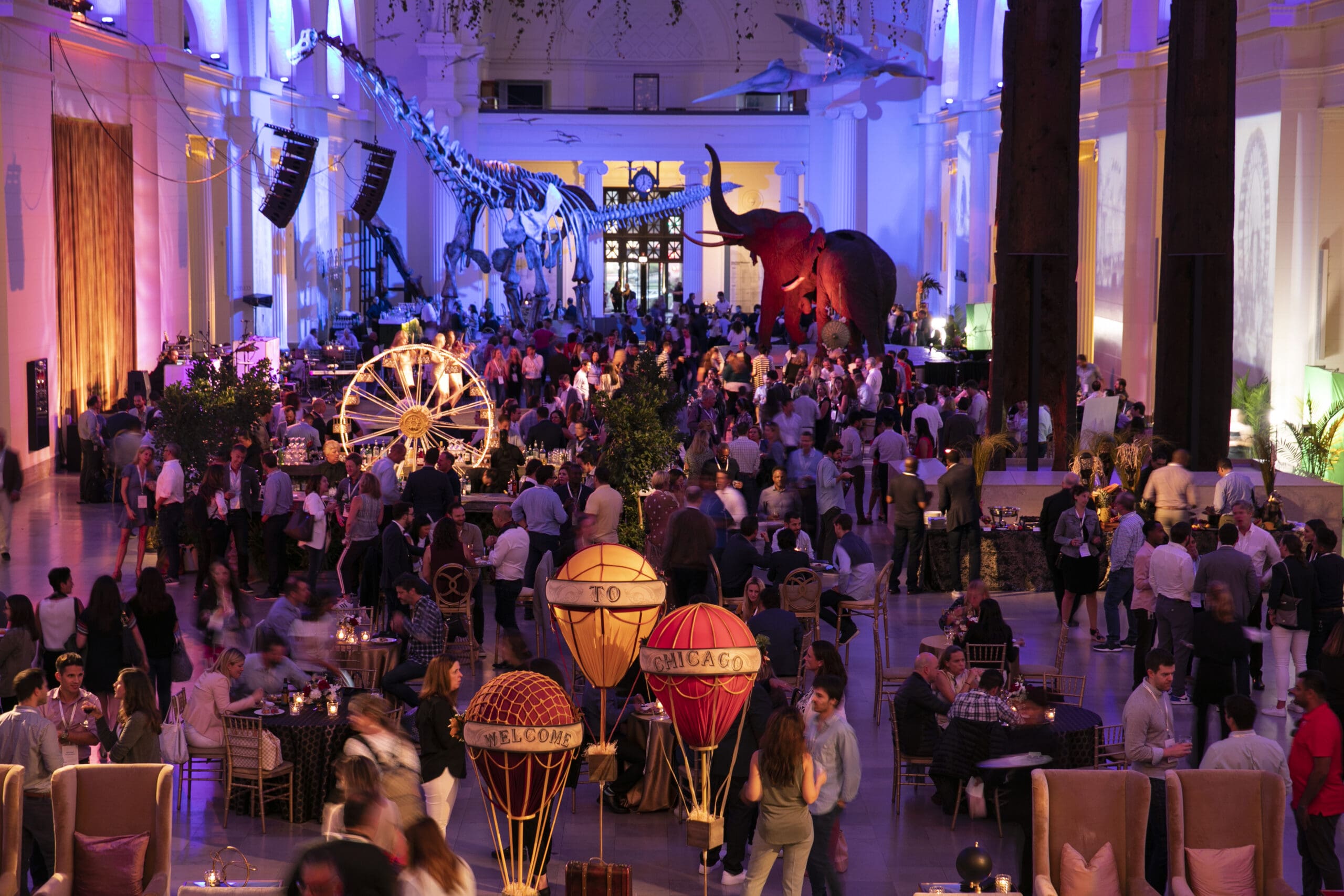 Large indoor corporate incentive event in a natural history museum with a dinosaur skeleton, mammoth and carnival decor