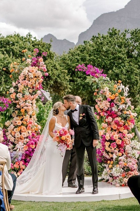 Sarah & Tom kissing between colourful floral columns at Vrede en Lust