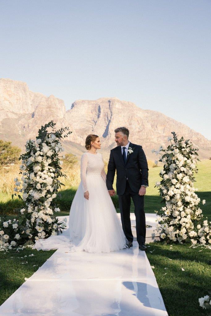 Celia & Grant at an outdoor altar with floral columns and mountains at Boschendal
