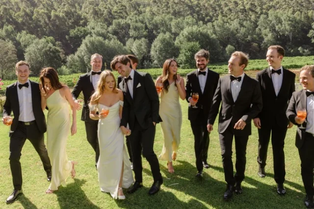 Wedding party laughing on a lawn, bridesmaids in yellow dresses
