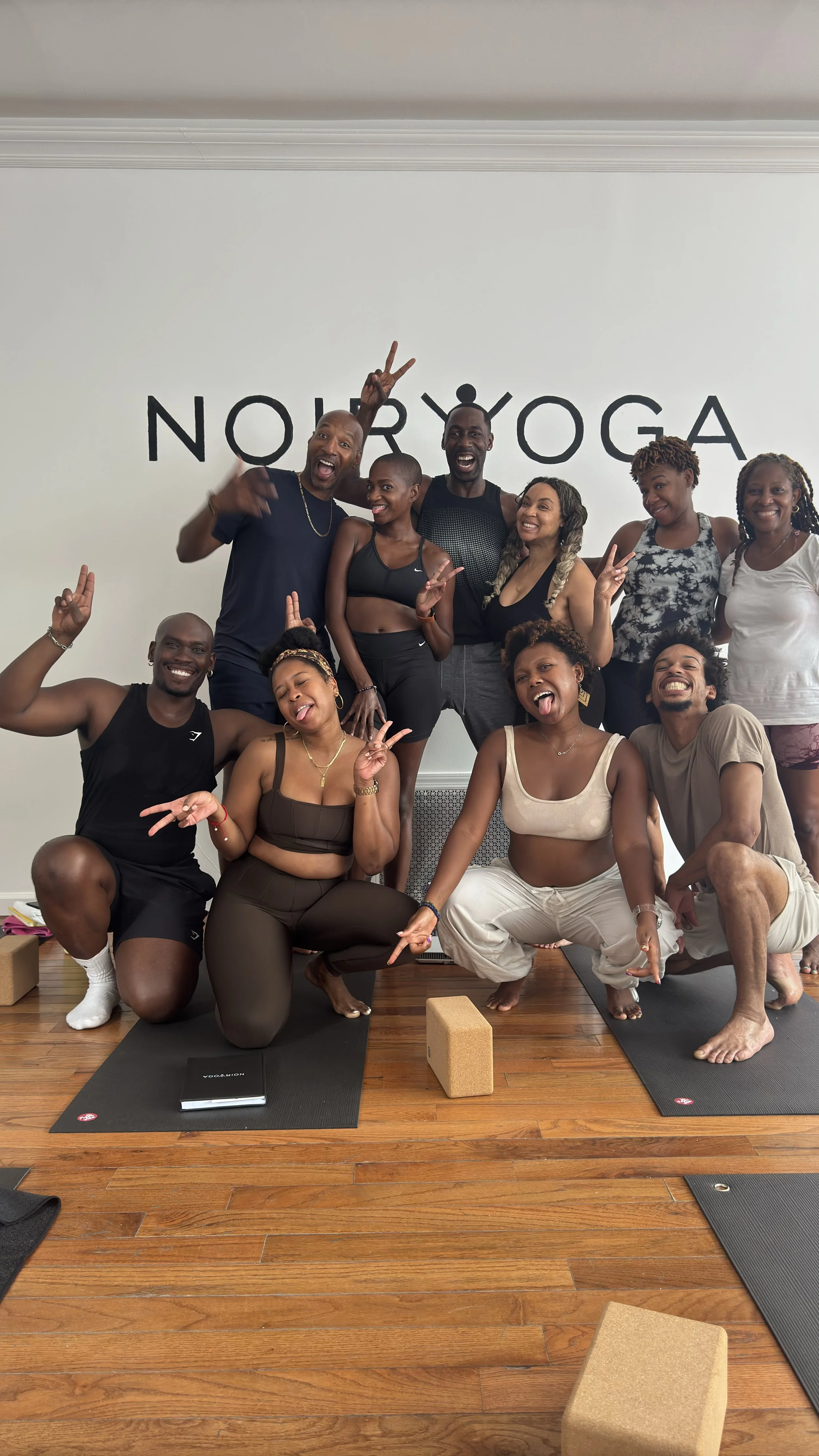 A group of people posing in front of the Noir Yoga logo in studio