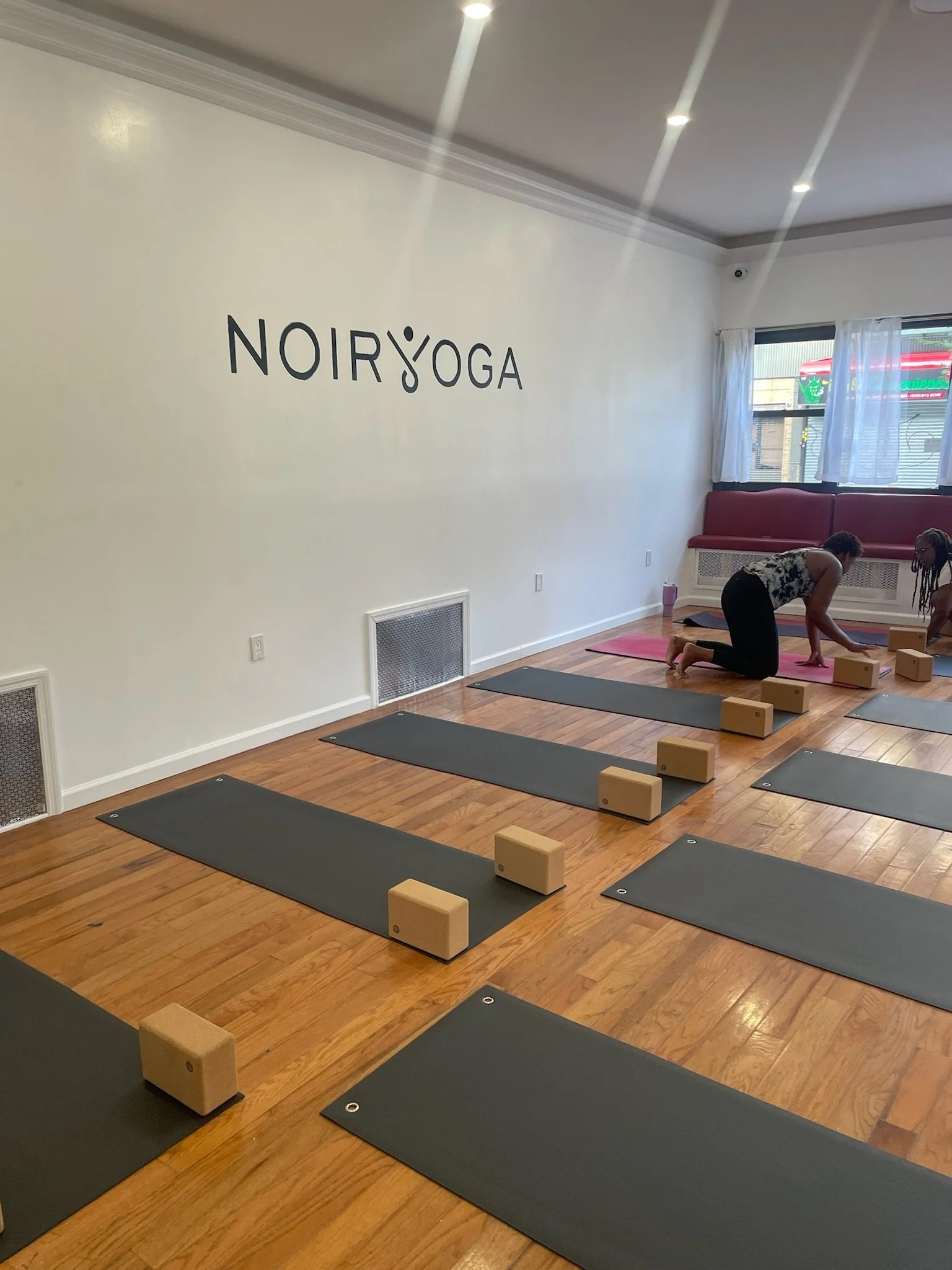 Mats and cork blocks set up in rows on the hardwood floor of the Noir Yoga studio