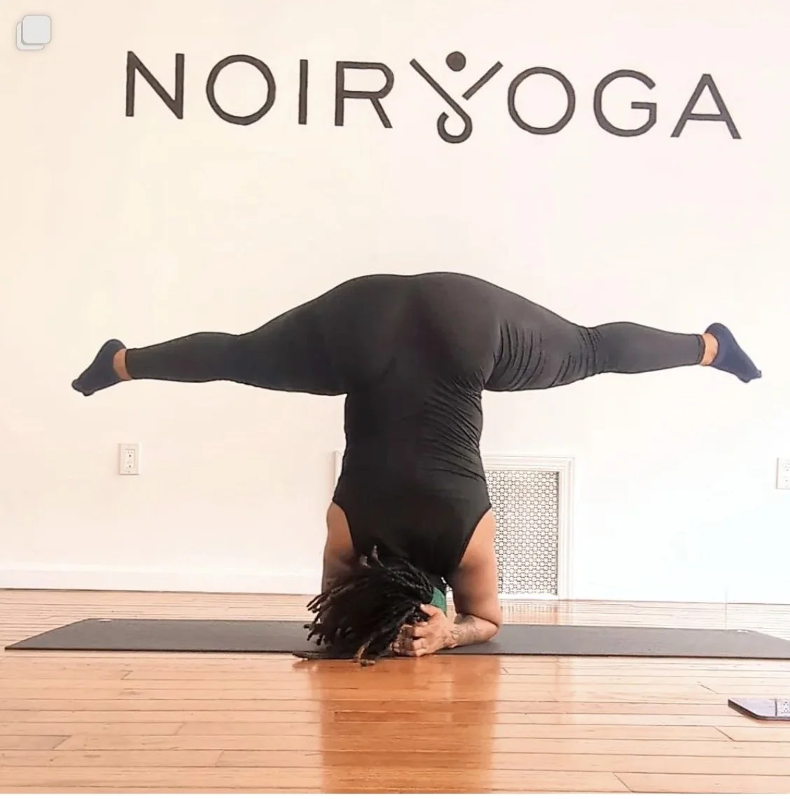 An instructor doing a headstand in front of the Noir Yoga logo