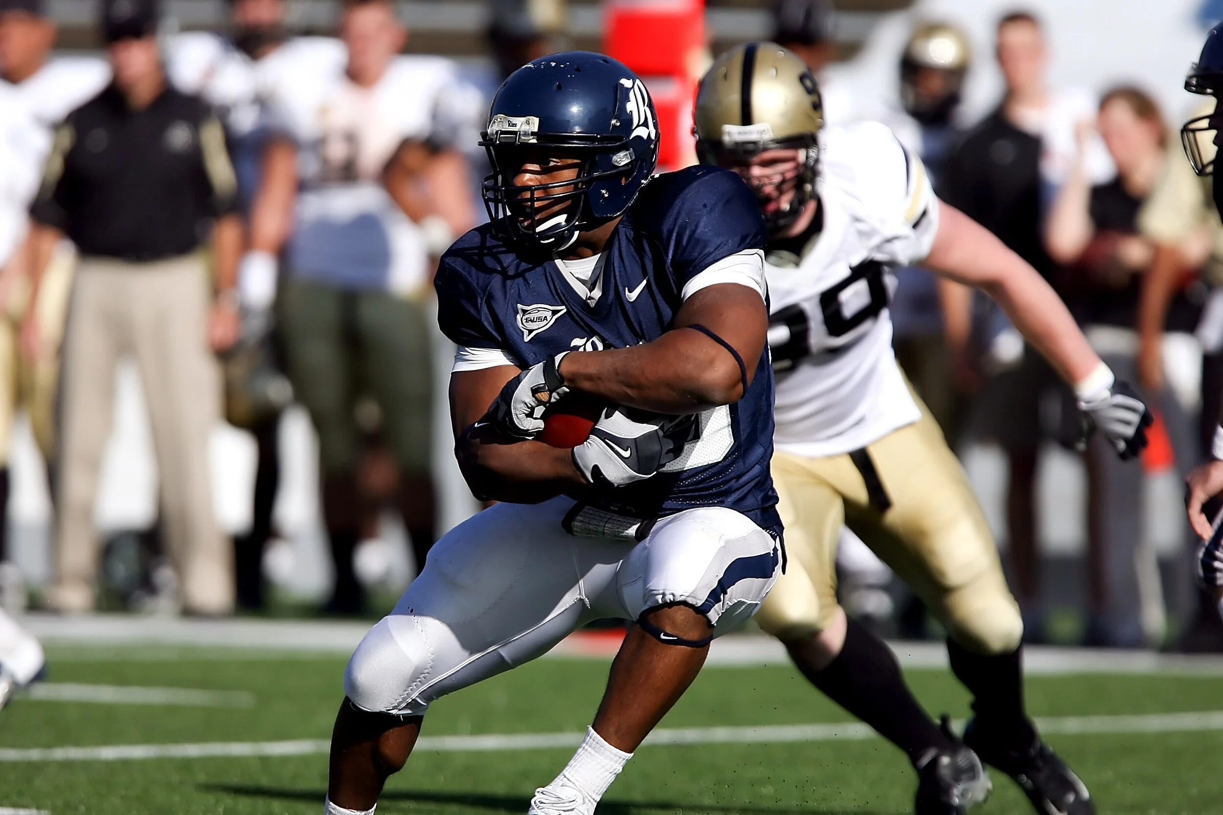 An American football player in a navy uniform running with the ball during a game