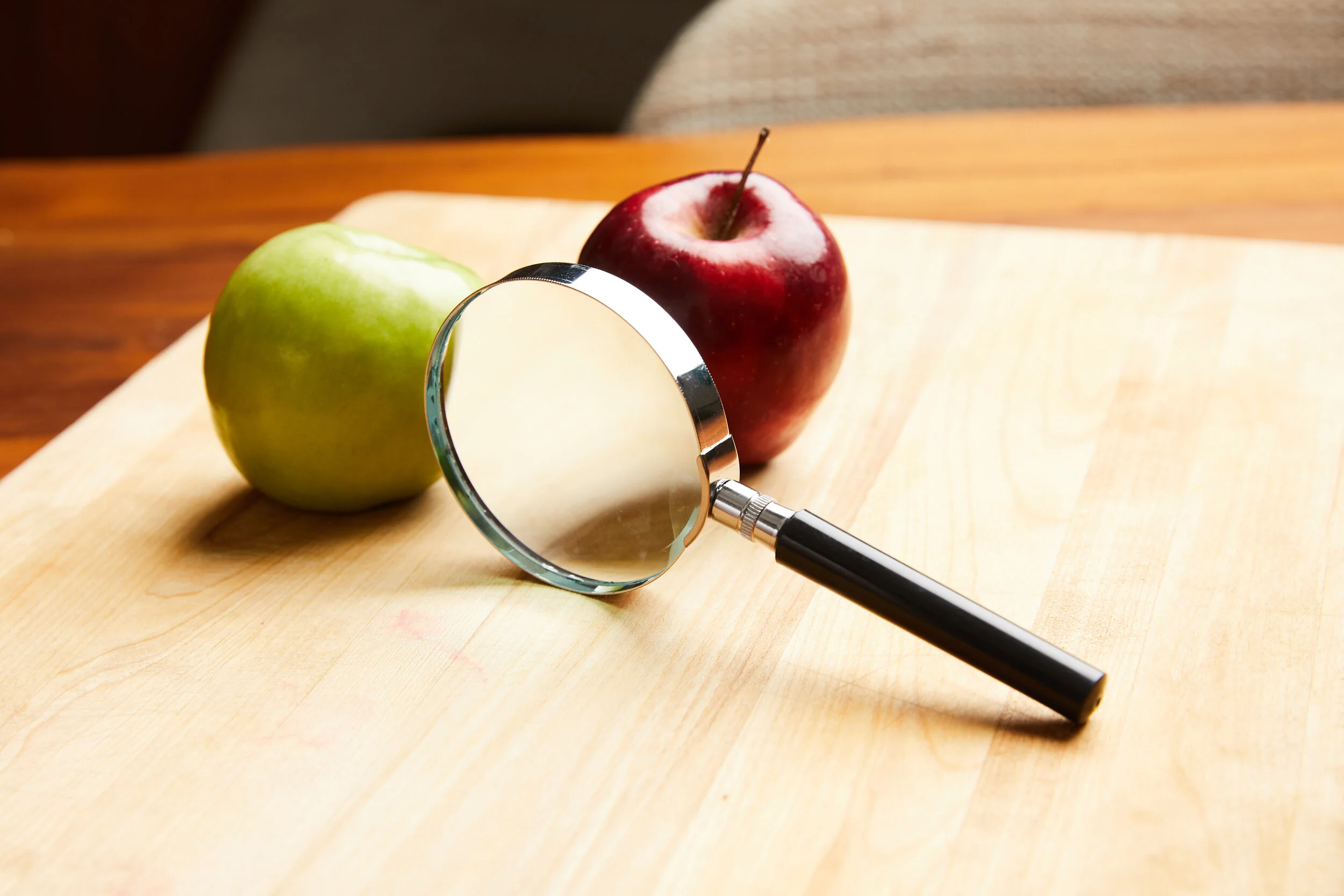 Green and red apples beside a magnifying glass on a wooden cutting board — the New Perspective Nutrition brand motif