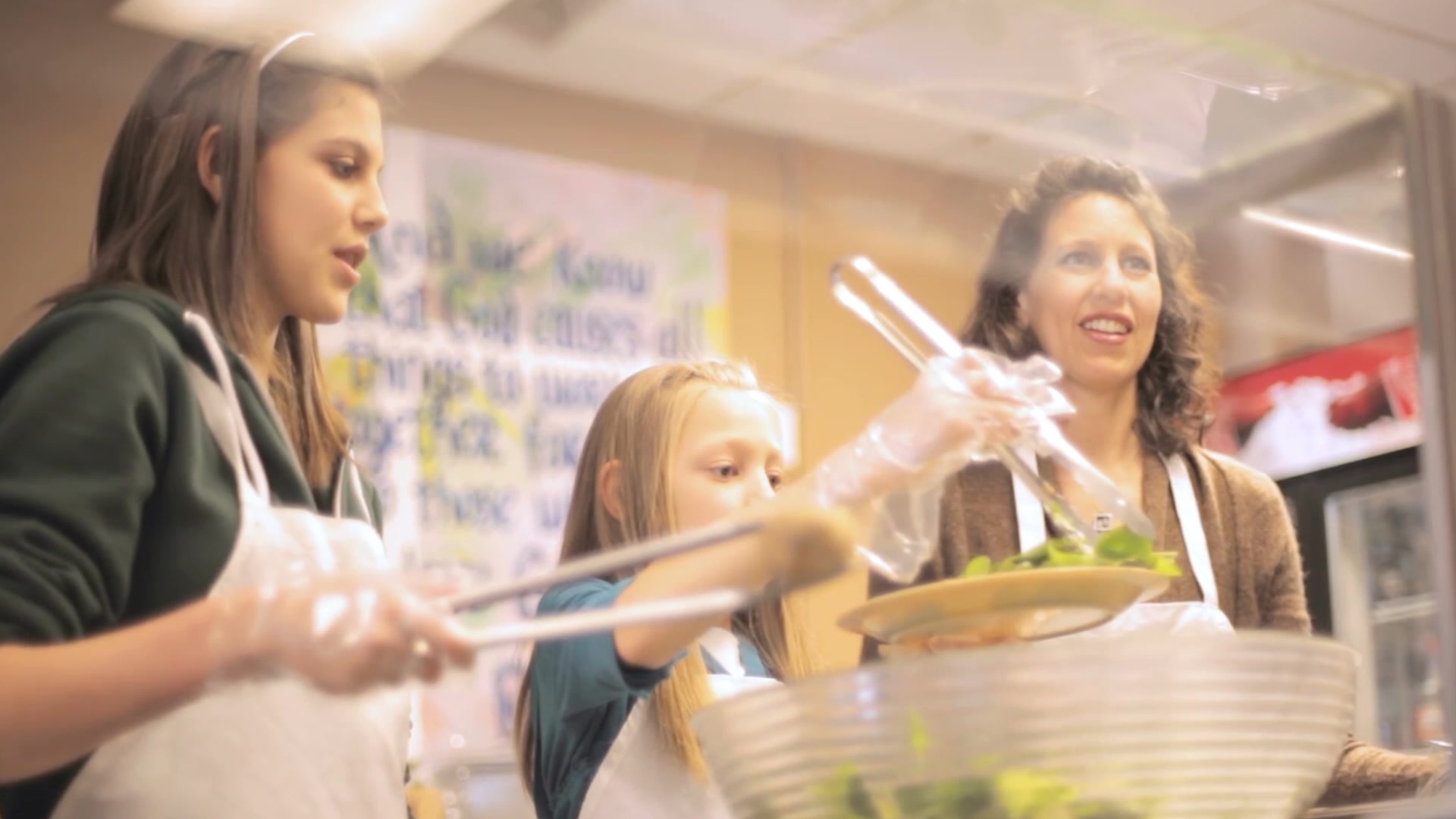 Two girls and a woman in aprons serving food at a community counter