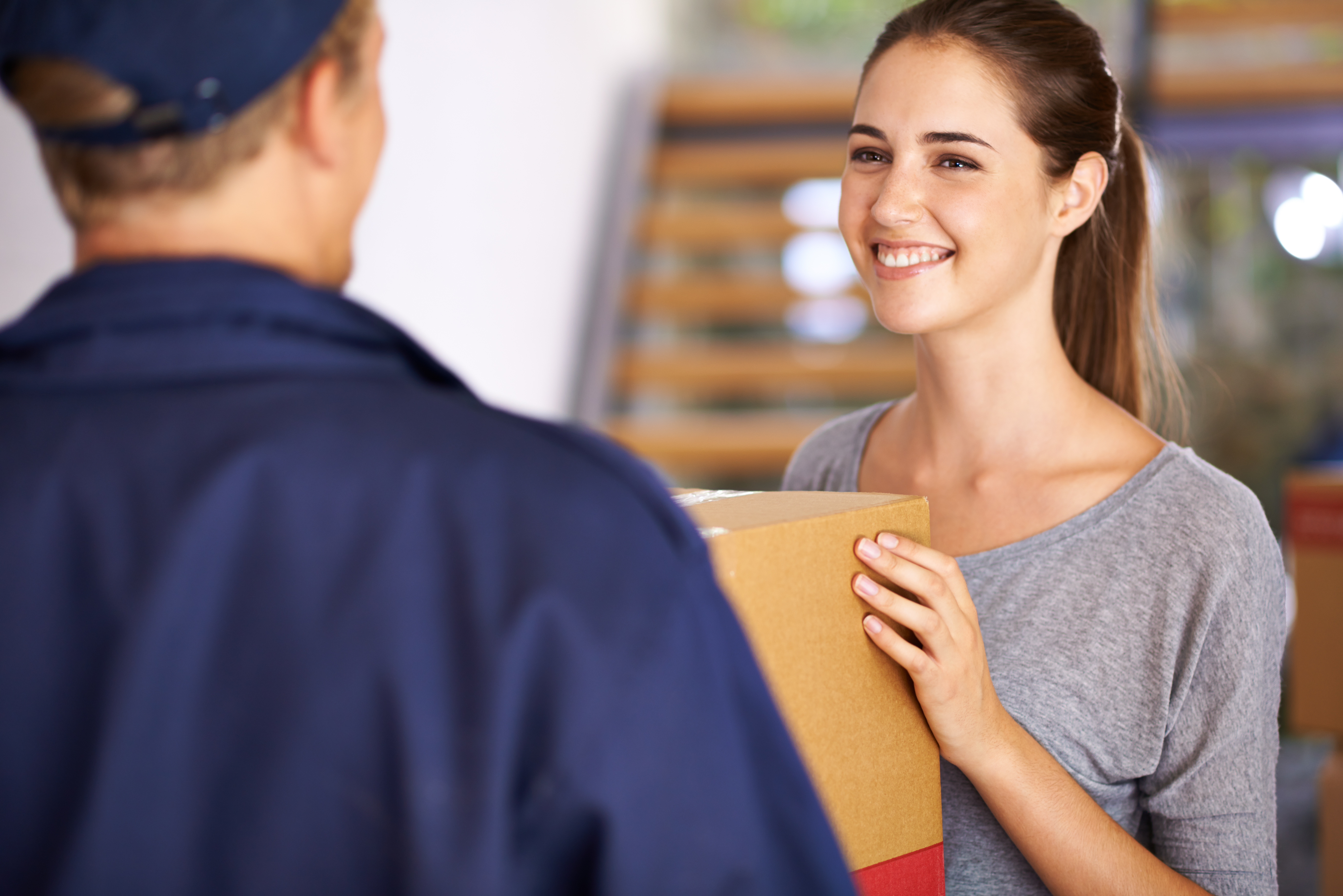 Smiling young woman receiving a cardboard package from a delivery person in a blue uniform