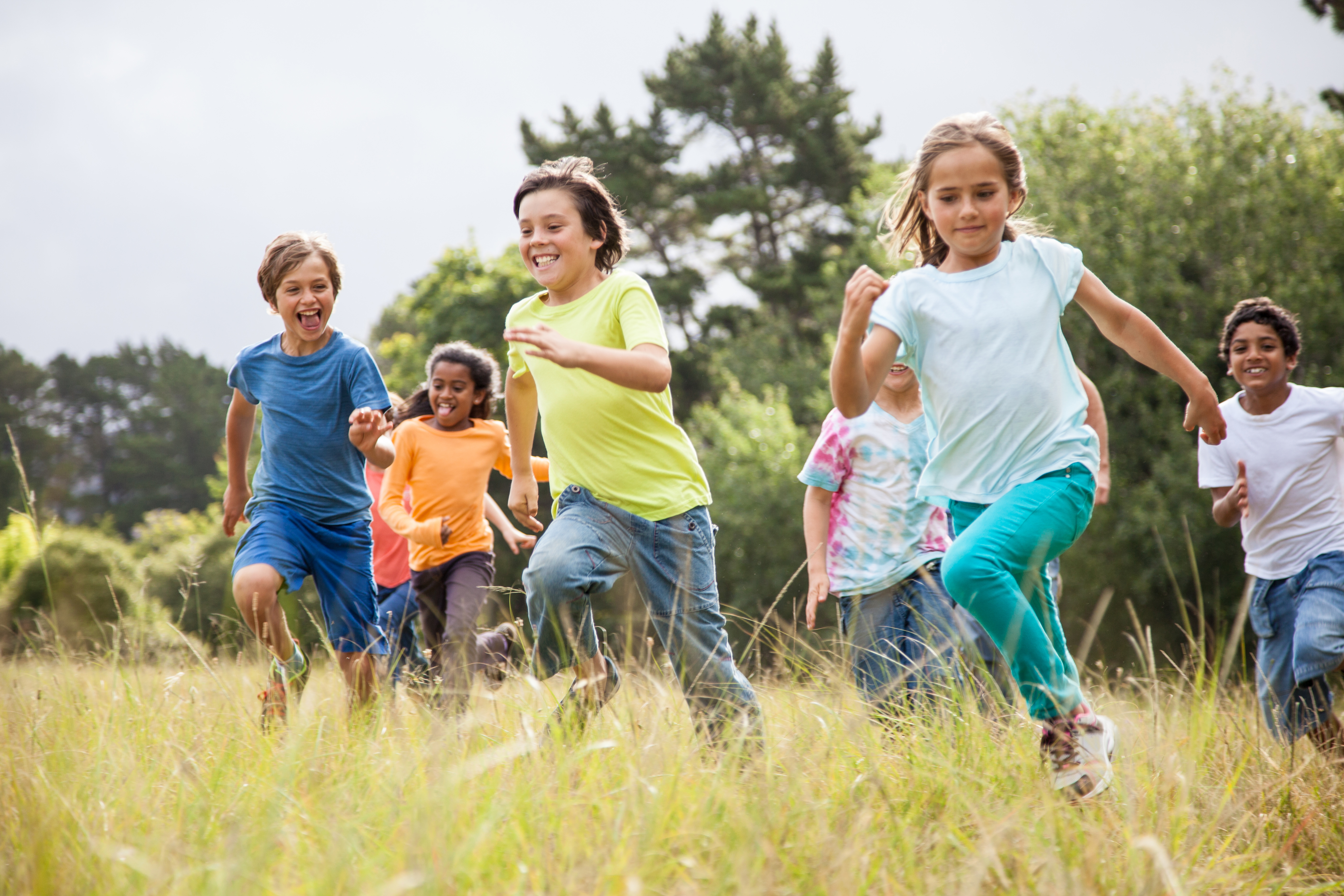 Group of diverse children running and laughing in a grassy field outdoors