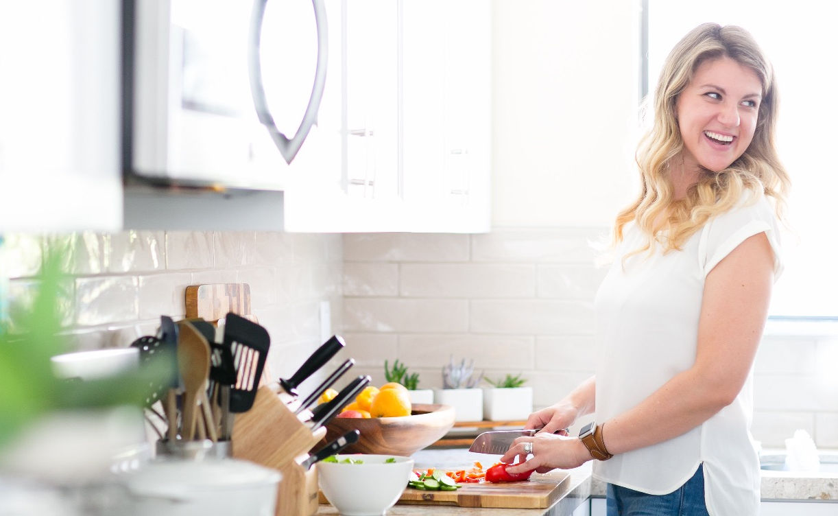 Smiling blonde woman chopping vegetables in a bright white kitchen