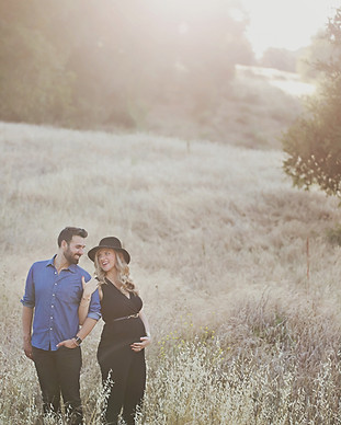 Pregnant couple standing in a golden sunlit field