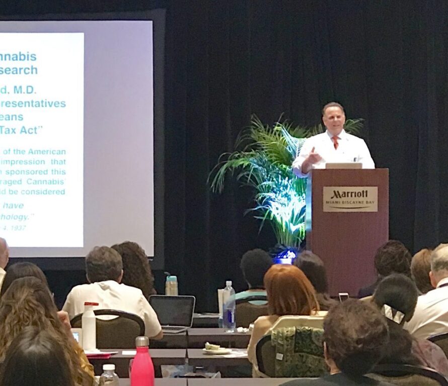 Dr. Block lecturing from a Miami Marriott Biscayne Bay podium to a full audience of clinicians, slides projected behind him