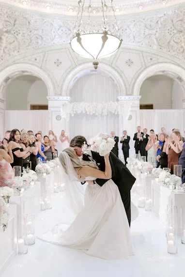 Groom dipping bride during their first dance in an ornate white ballroom