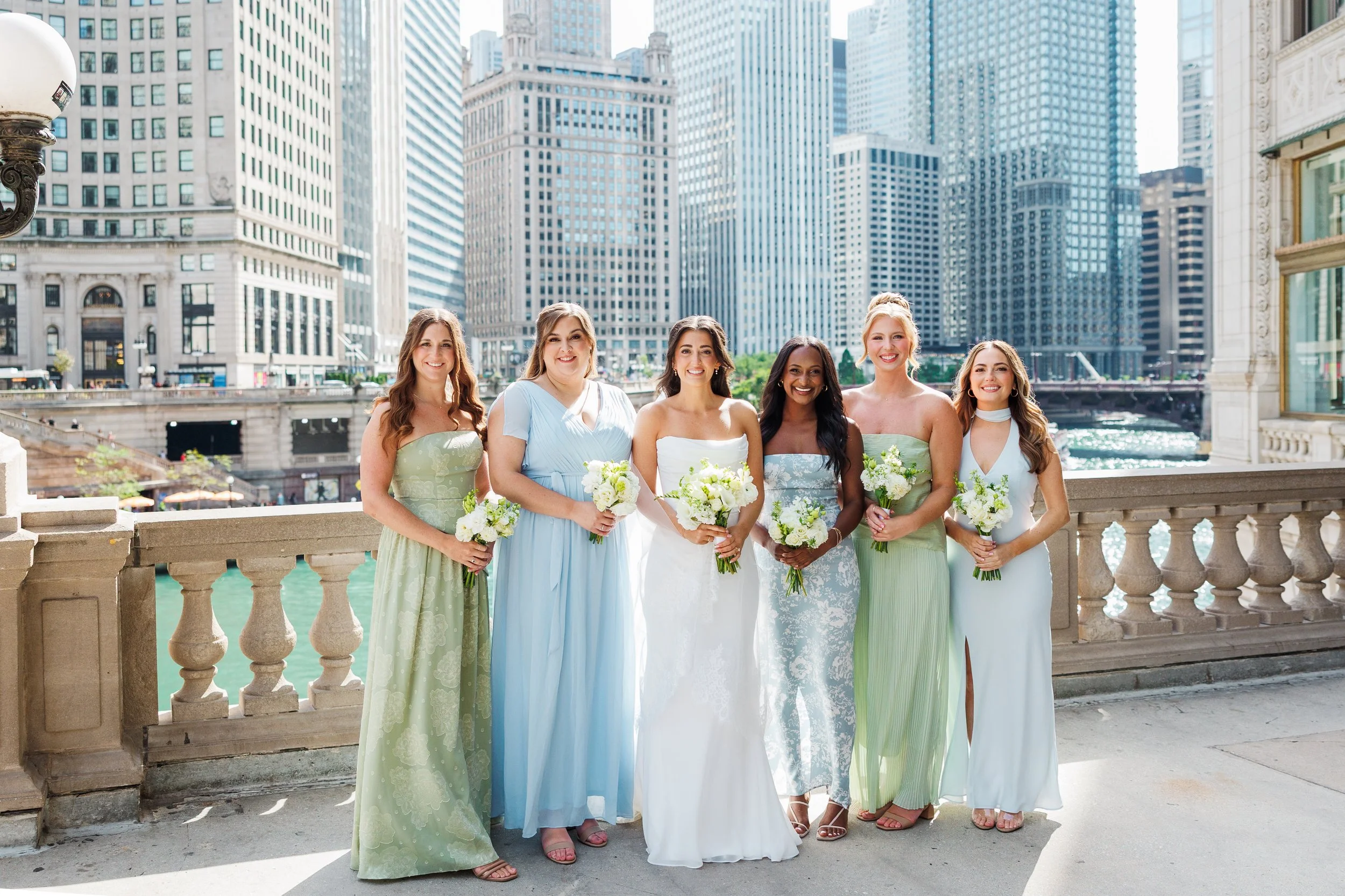 Bride with five bridesmaids in sage and blue gowns on a river terrace