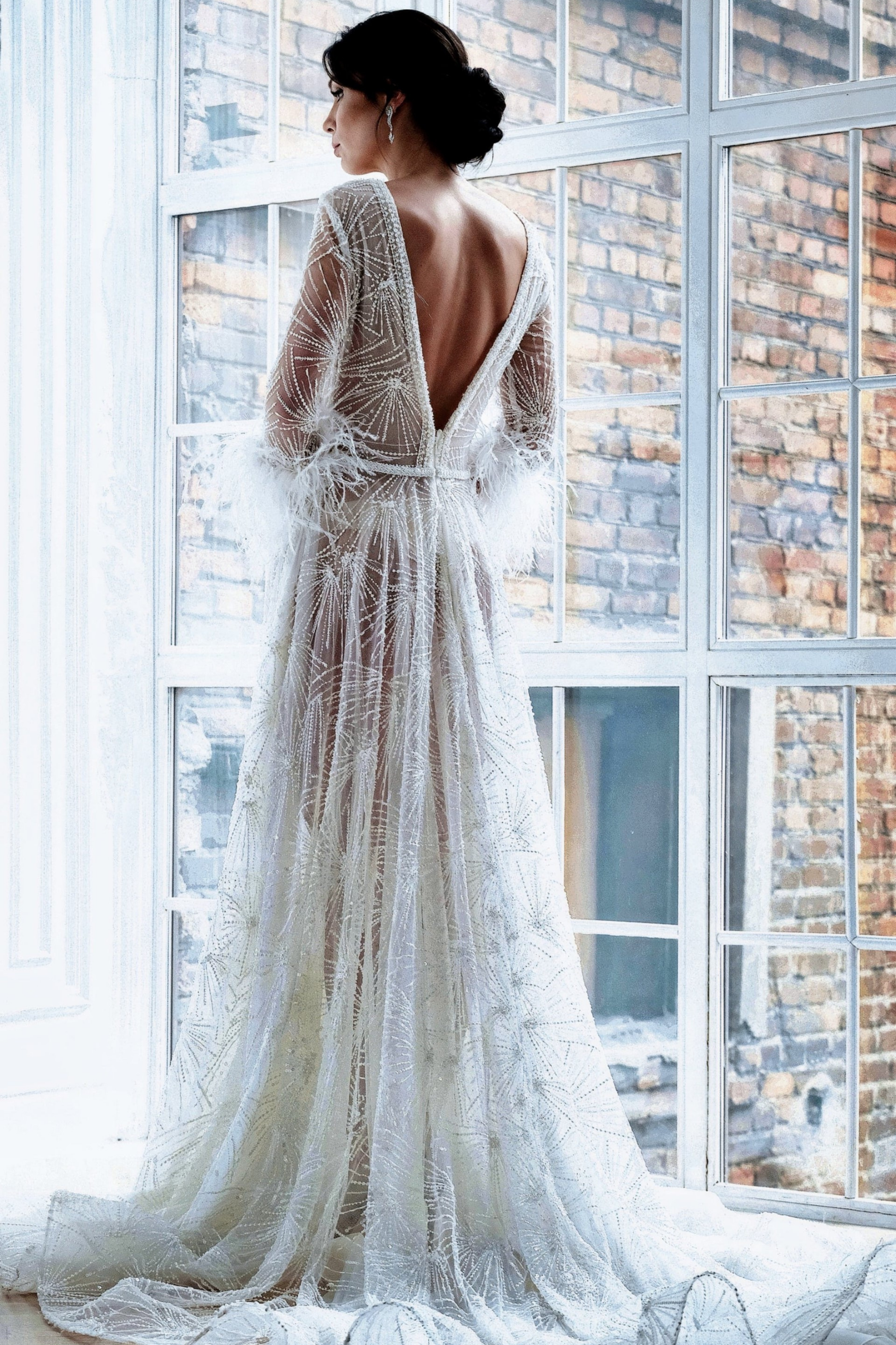 Bride in beaded lace gown gazing out a large factory window