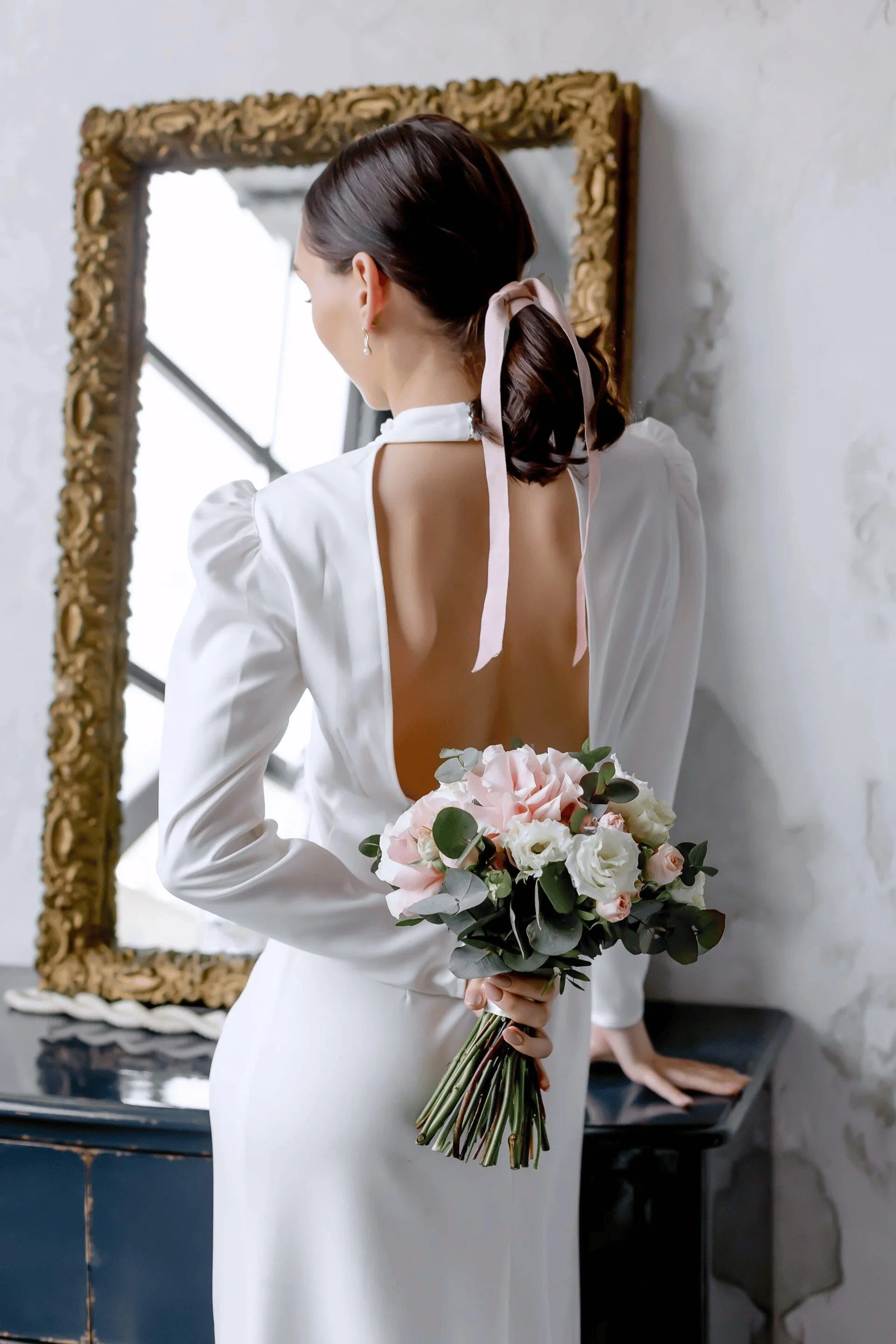 Bride holding a blush bouquet, facing a gold ornate mirror