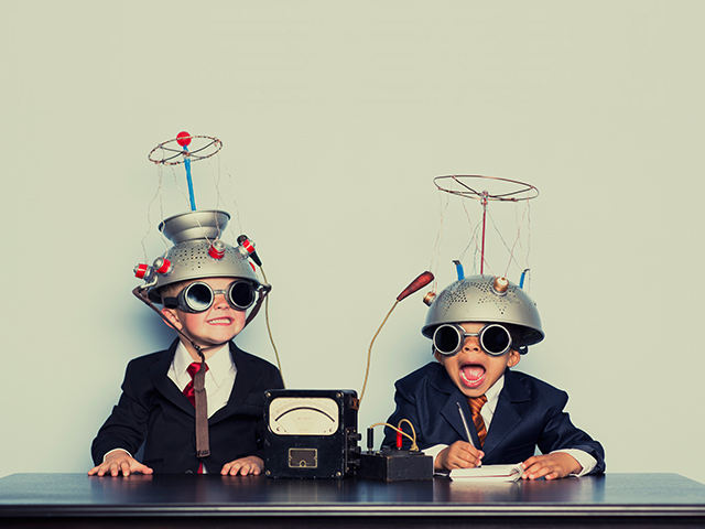 Two young children in suits wearing homemade mind-reading helmets at a desk