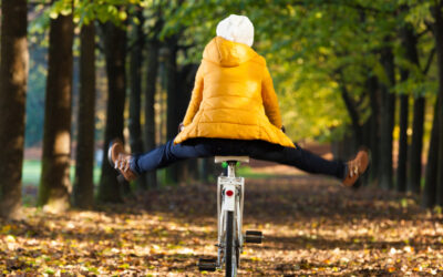 Person in a yellow jacket riding a bicycle with feet out on an autumn path