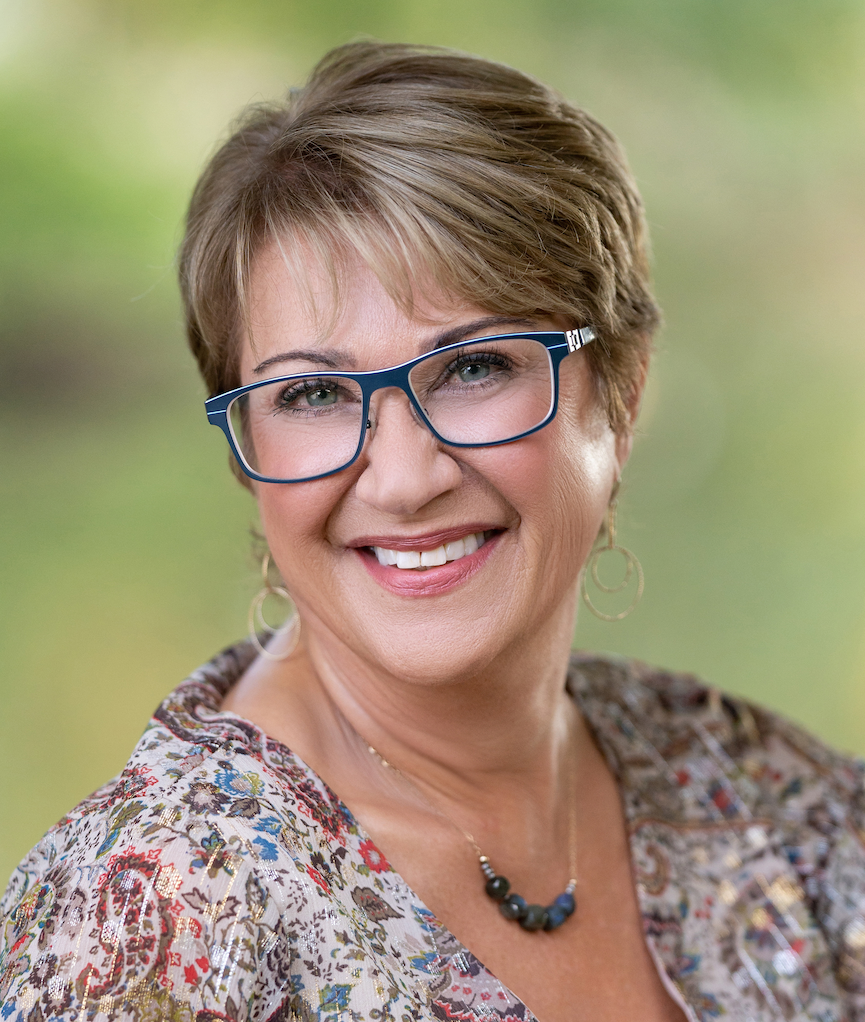 Tracy Benson, executive coach, smiling in blue glasses against a green background