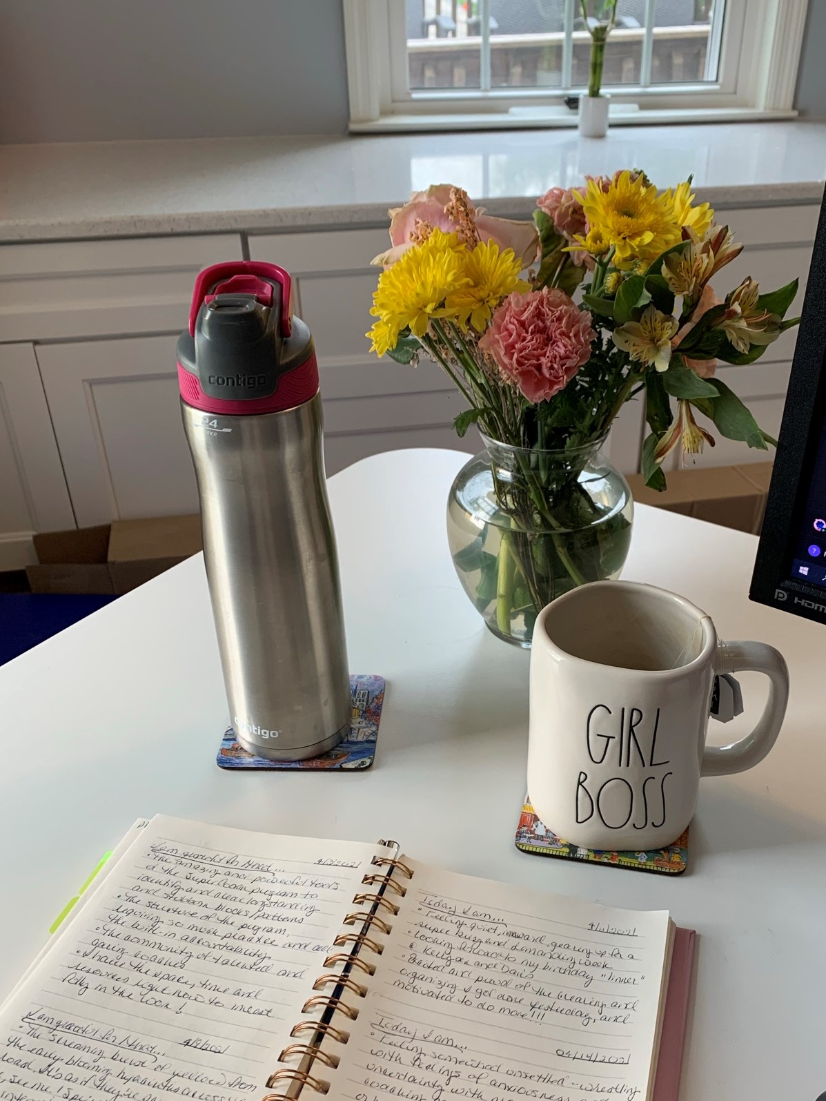 Desk flatlay: a Girl Boss mug, water bottle, flowers and an open journal with handwritten notes