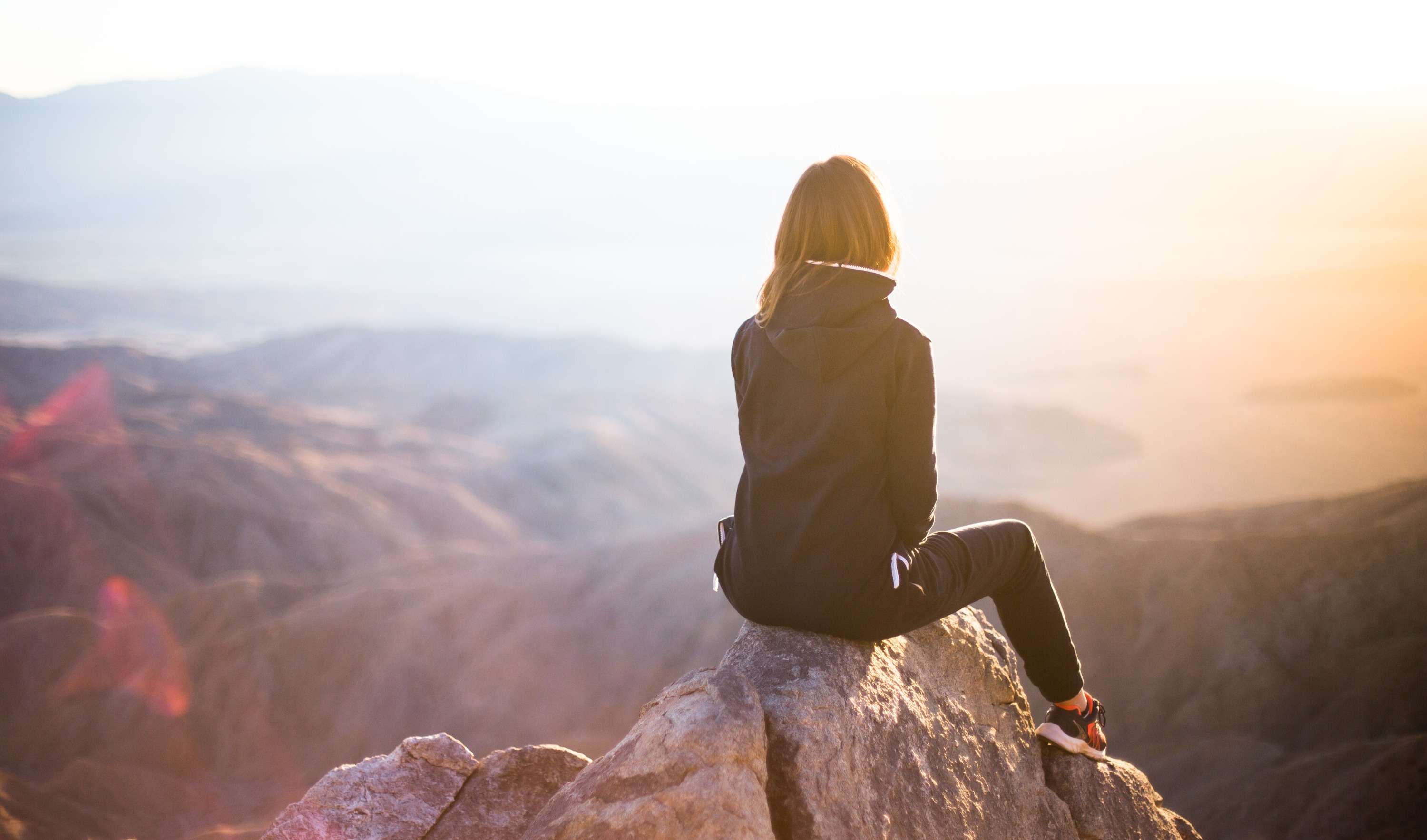 Woman sitting on a mountain summit overlooking a valley at sunset