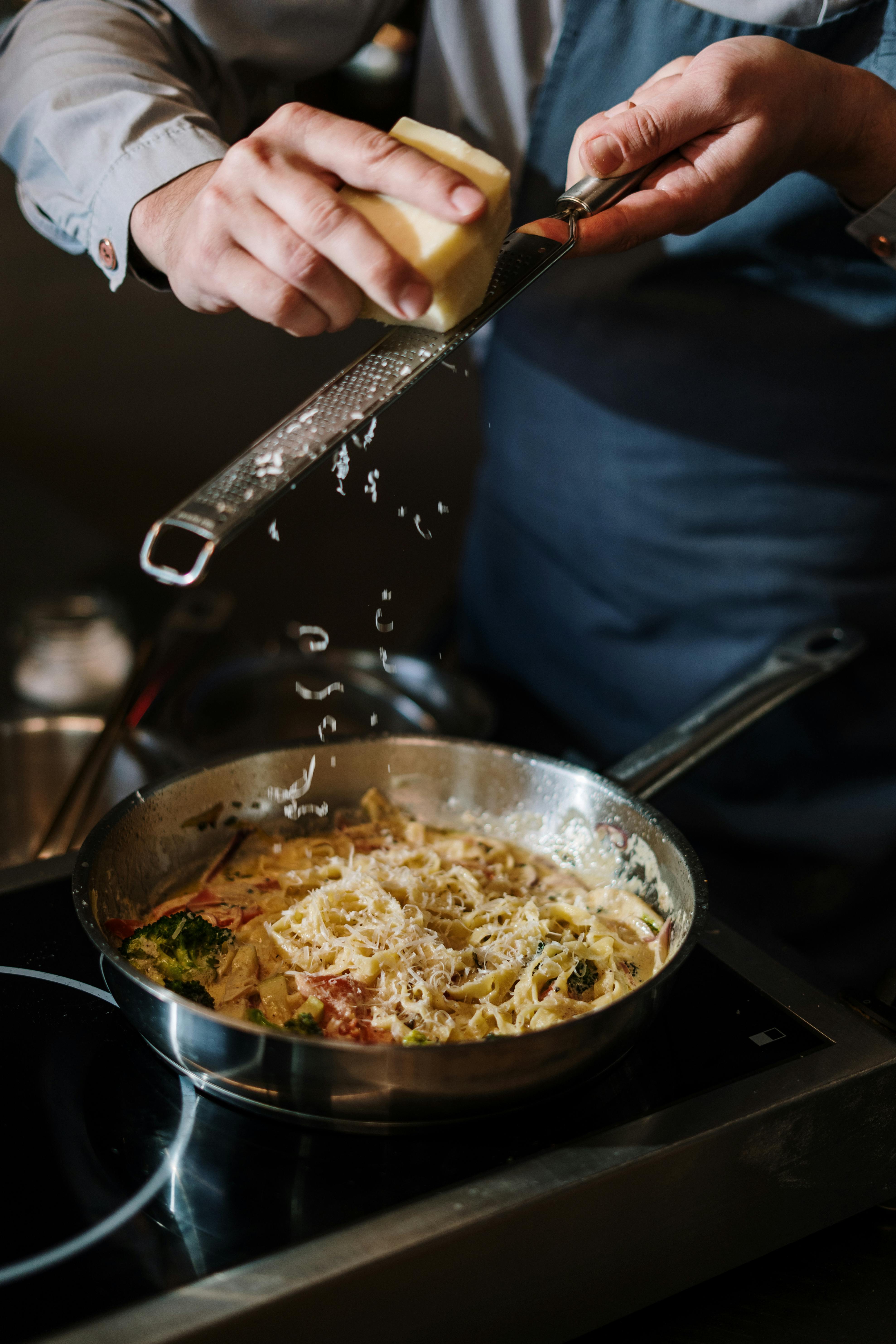 Chef grating Parmigiano Reggiano over a pan of creamy pasta