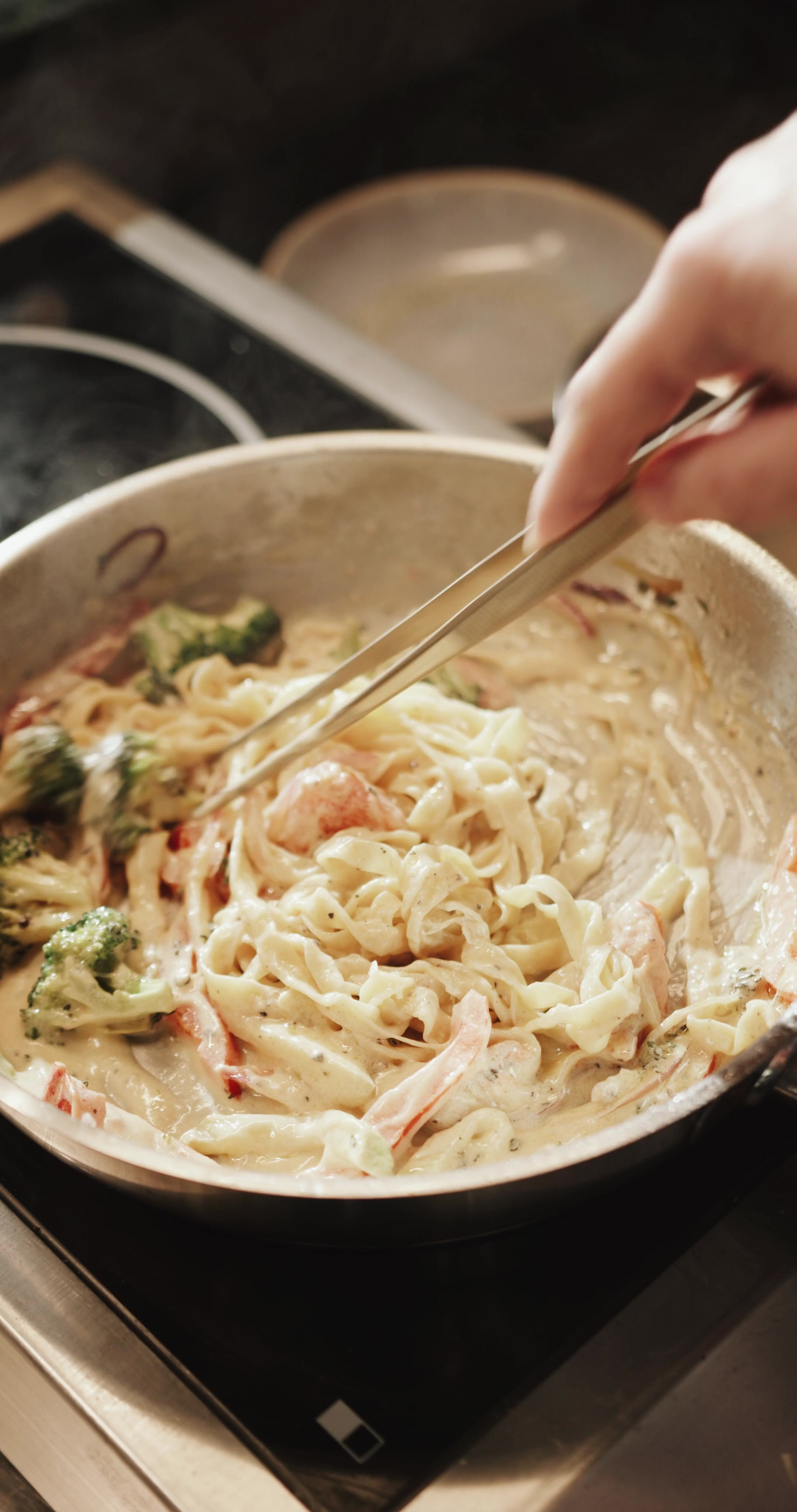 Creamy fettuccine with broccoli and red peppers stirred with tongs, overhead