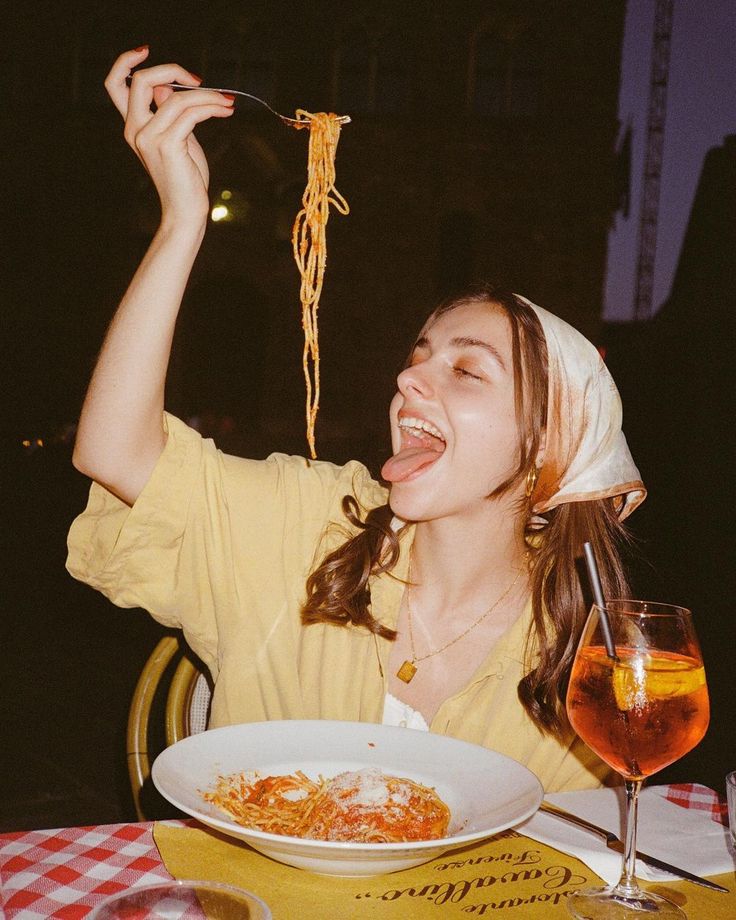 Young woman joyfully eating spaghetti at an outdoor table with a spritz