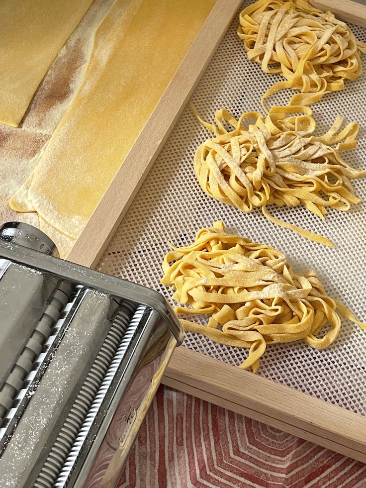 Fresh tagliatelle nests drying on a rack beside a manual pasta machine