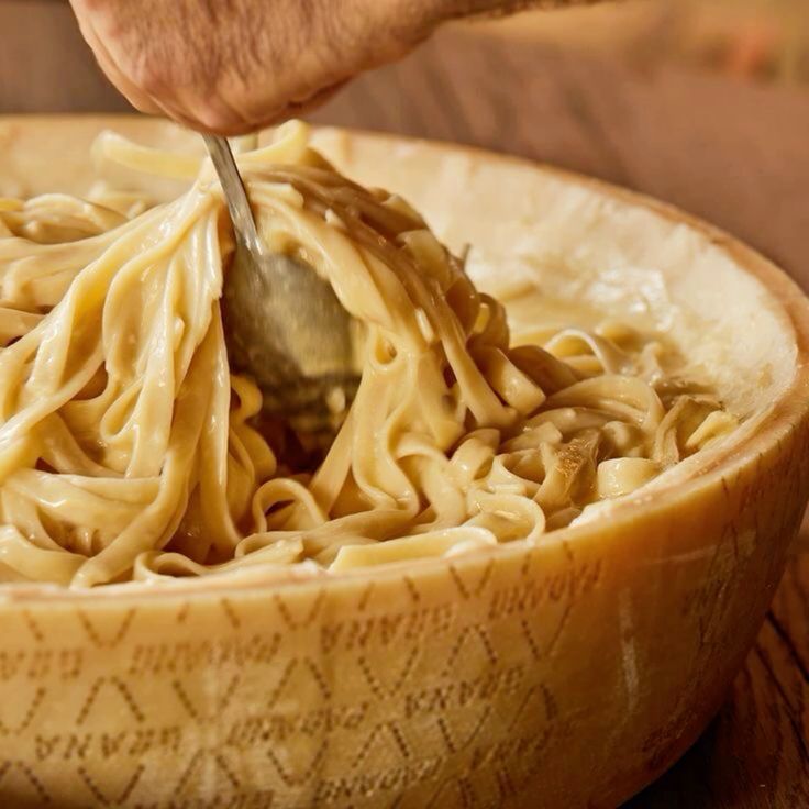 Pasta being tossed inside a hollowed-out giant wheel of Parmigiano Reggiano