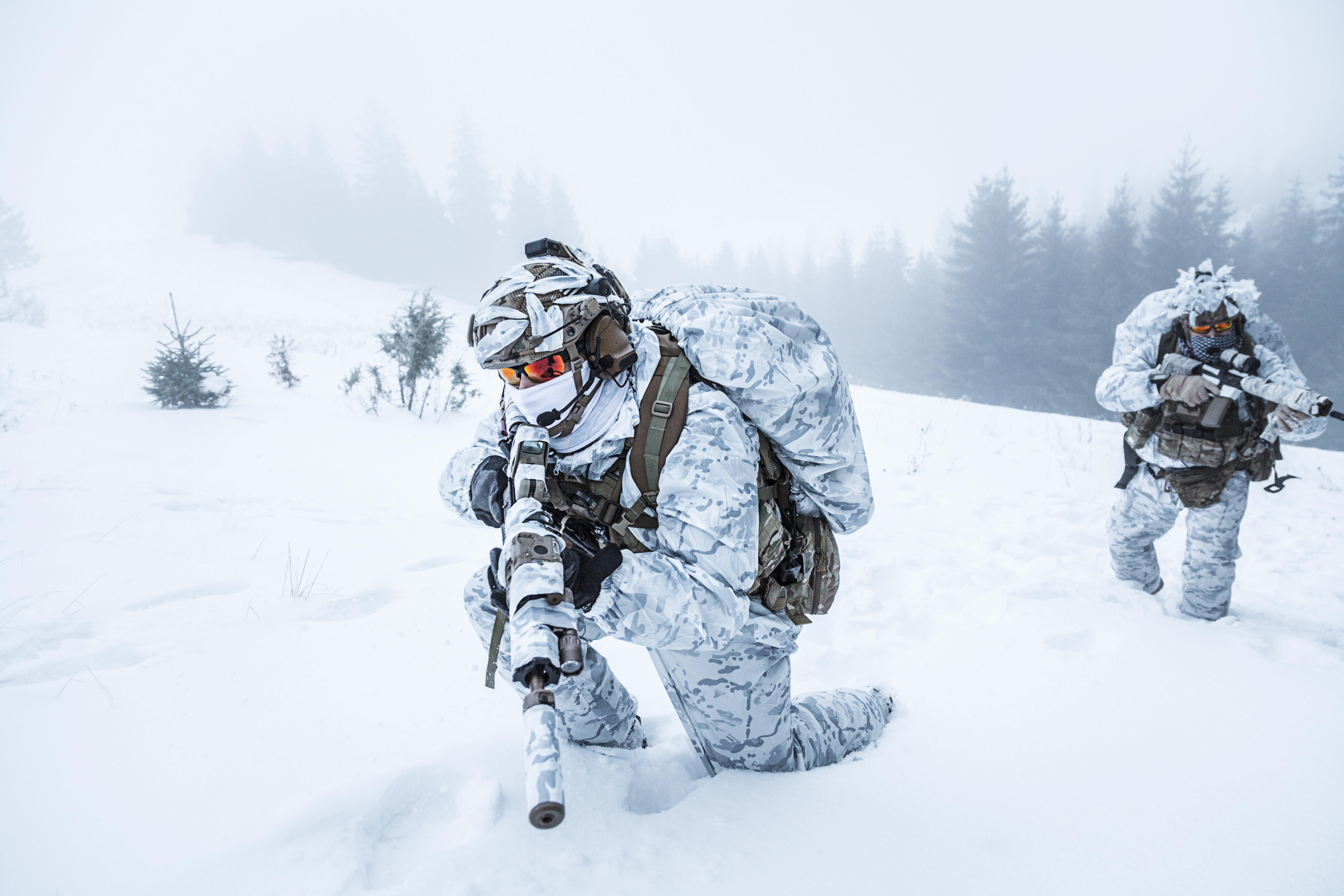 Two soldiers in white winter camouflage advancing through foggy mountain snow