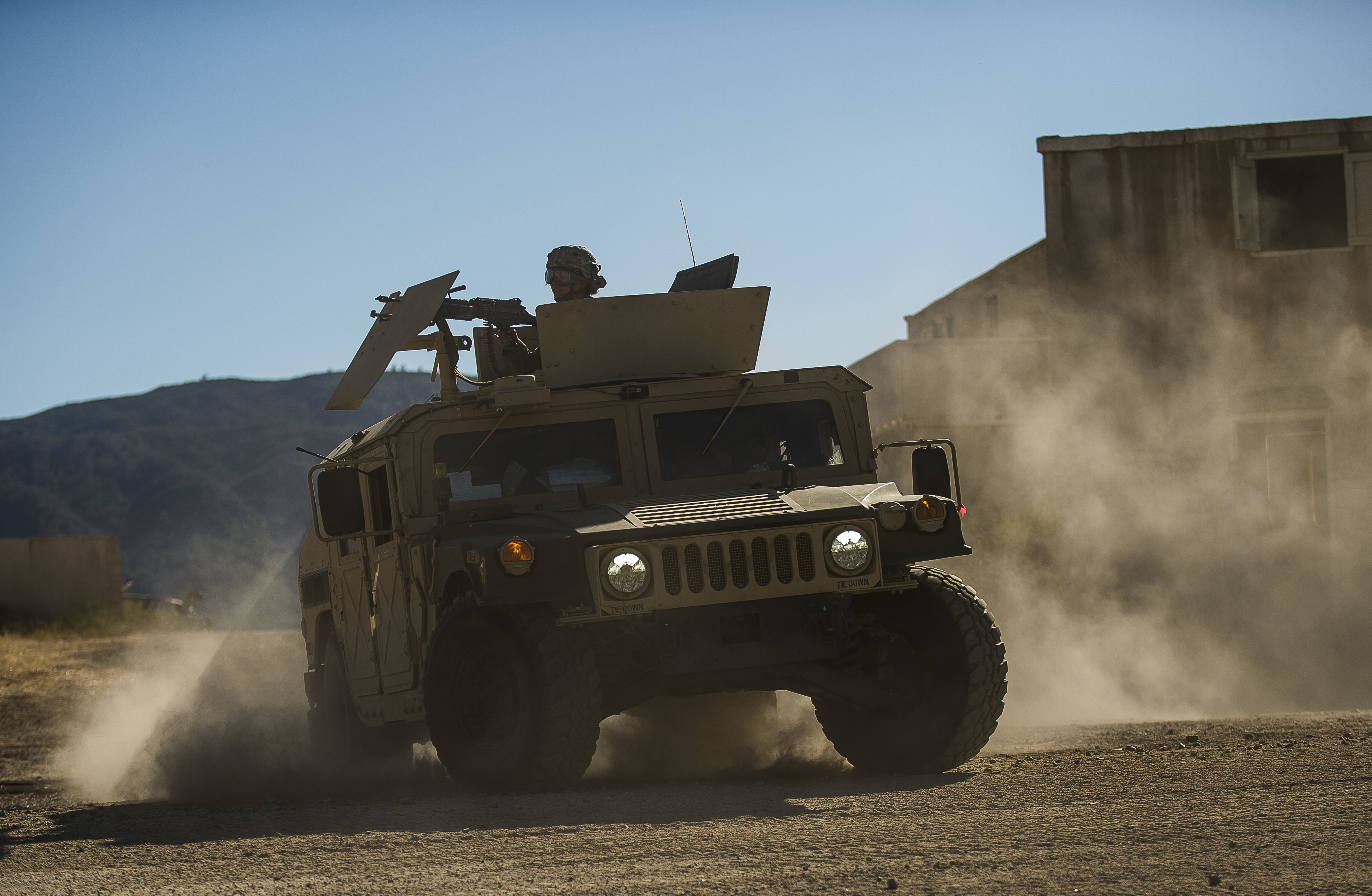 Military Humvee driving through dusty desert terrain with a soldier in the turret