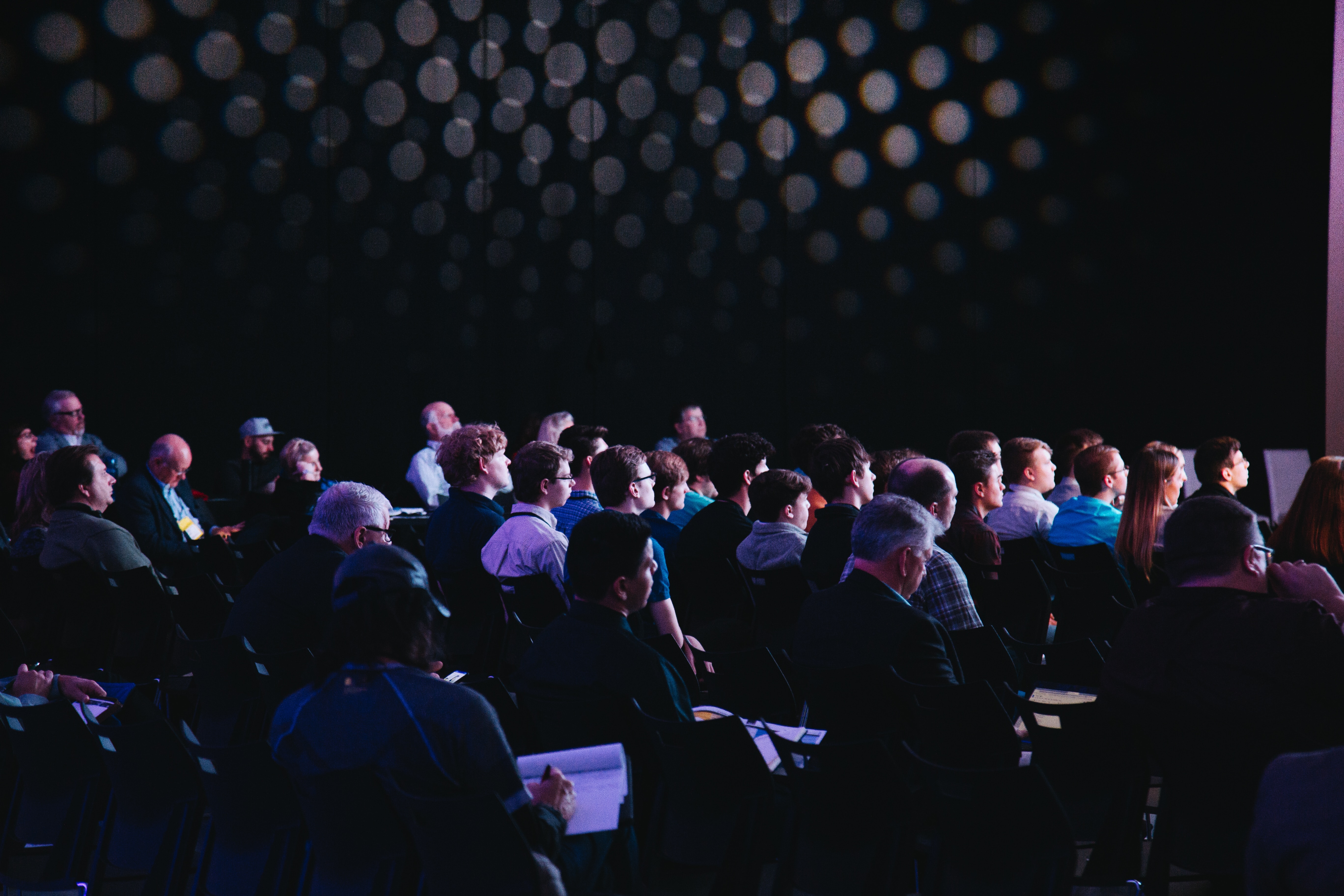 Audience seated in a darkened keynote venue under blue and purple stage lighting