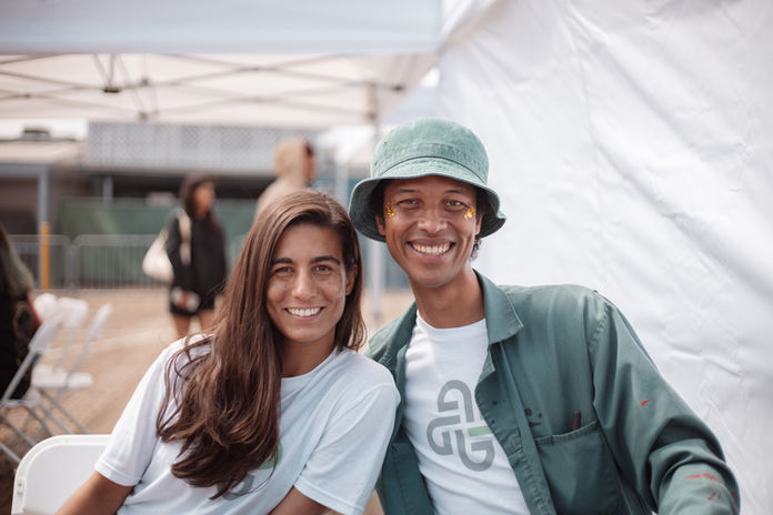 Two smiling people posing together, one in a green bucket hat, at an outdoor event