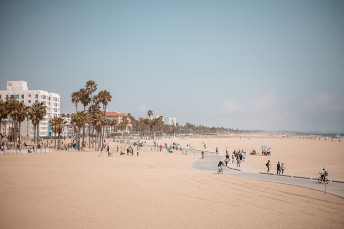 Wide shot of the Santa Monica boardwalk and sand with palm trees and cyclists