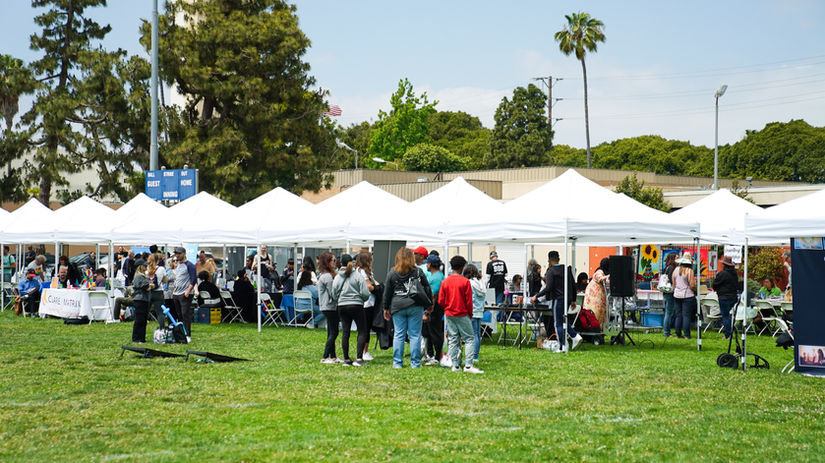 Outdoor community health fair with white tents, attendees and palm trees