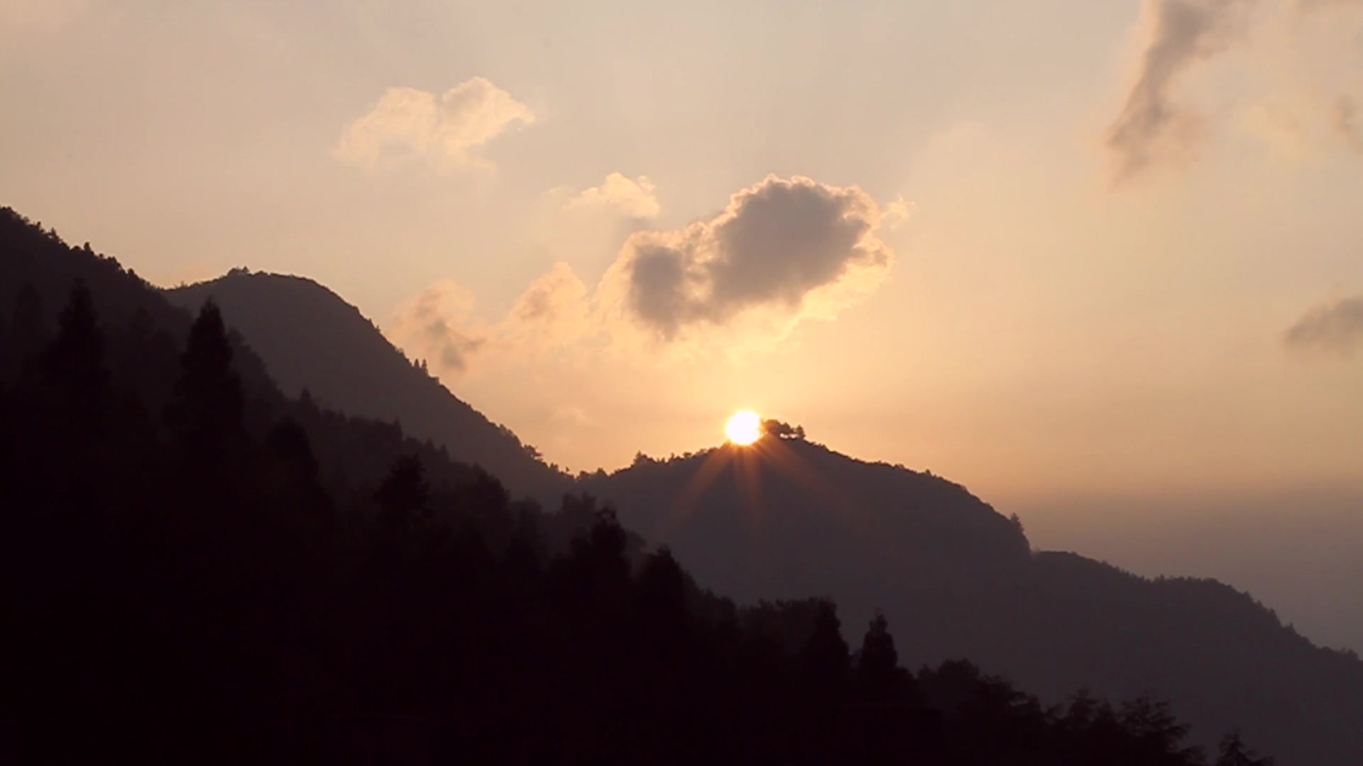 Mountain silhouette at sunset with sun bursting through clouds