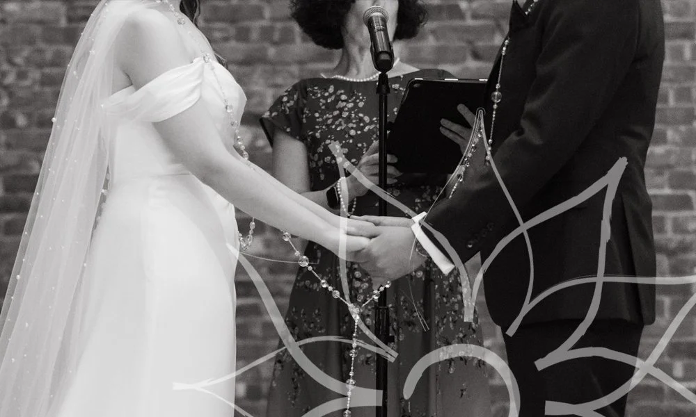 Black-and-white photo of a couple holding hands at the altar with officiant in the background