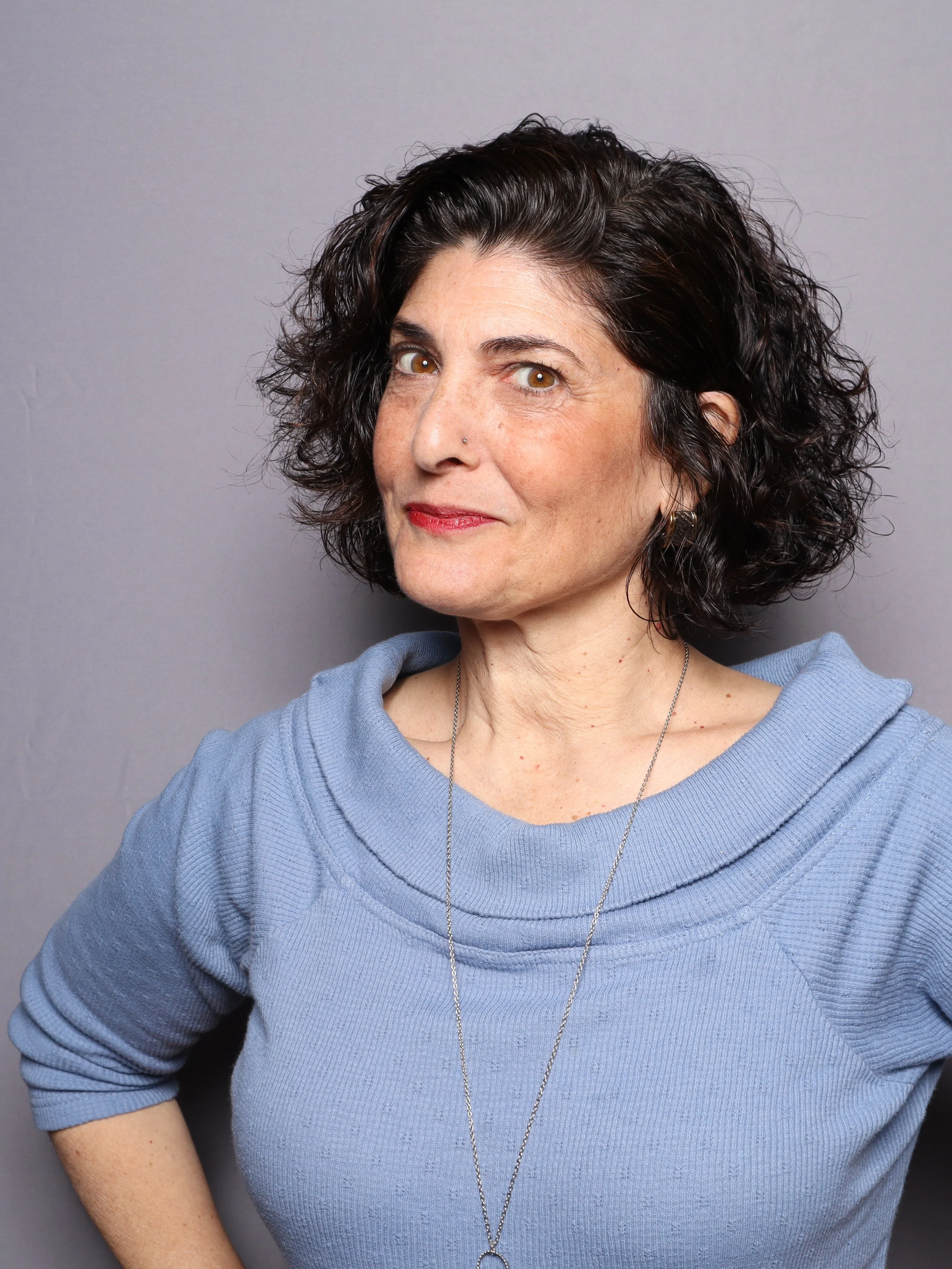 Hope Mirlis, curly dark hair, blue top and long necklace, professional portrait