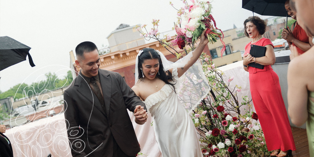 Rooftop wedding recessional with a joyful bride raising her bouquet and officiant clapping