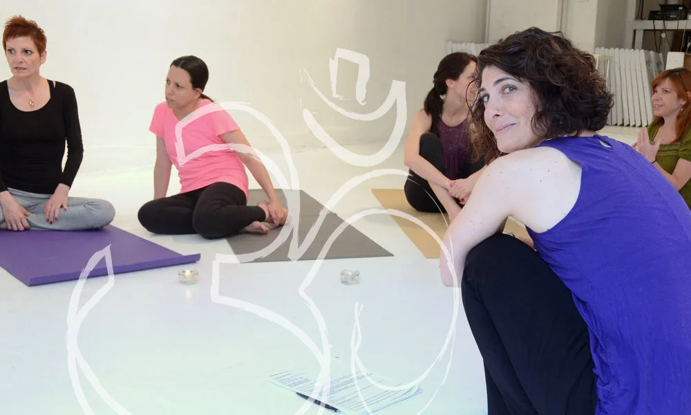 An instructor sitting with a small group of women on mats in a bright studio